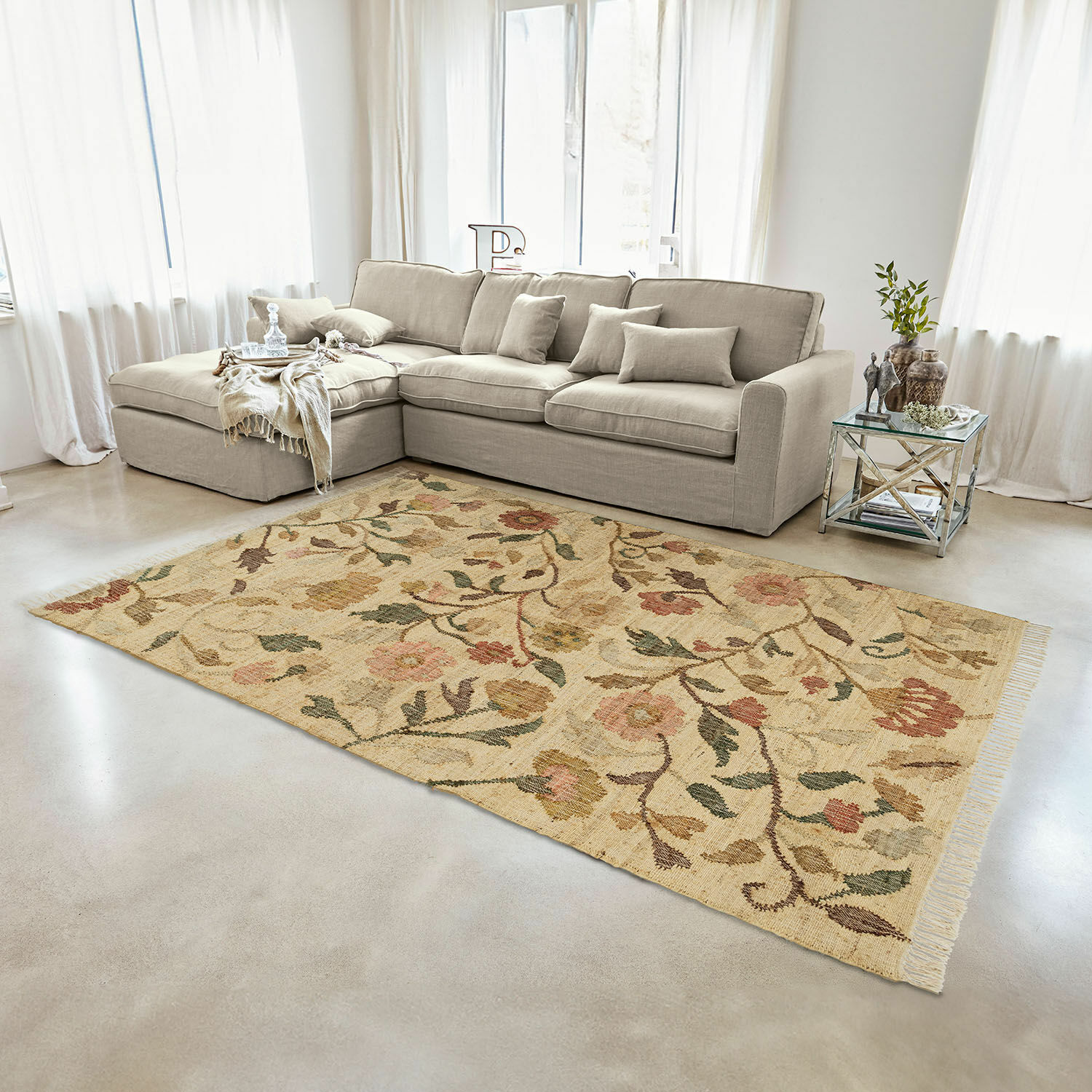 Teppich Théranelle Beiger Wollteppich mit floralem Muster im Wohnzimmer mit grauem Sofa und Glastisch.