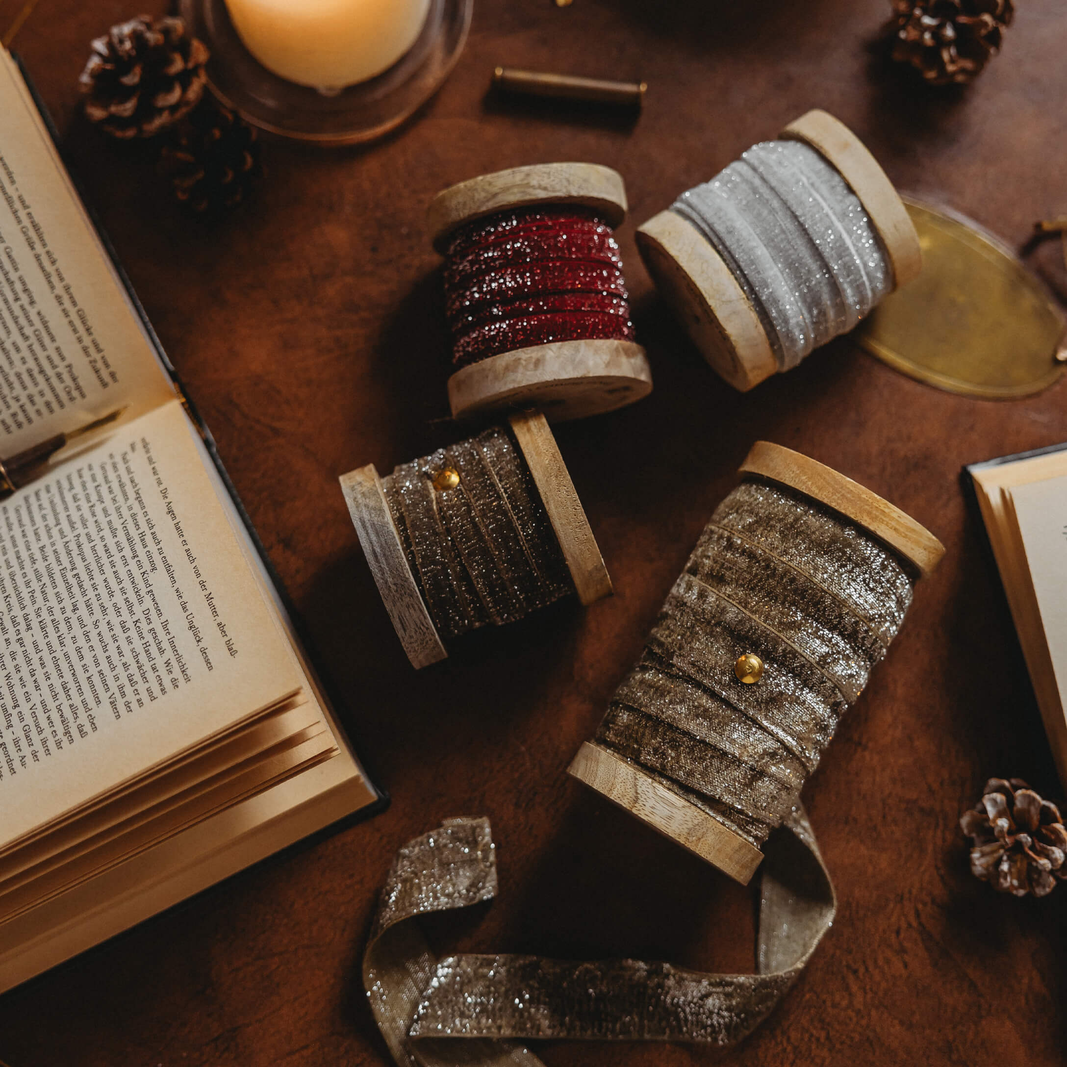 Holzspulen mit glitzernden Bändern in Rot, Silber und Gold auf einem Tisch mit Büchern