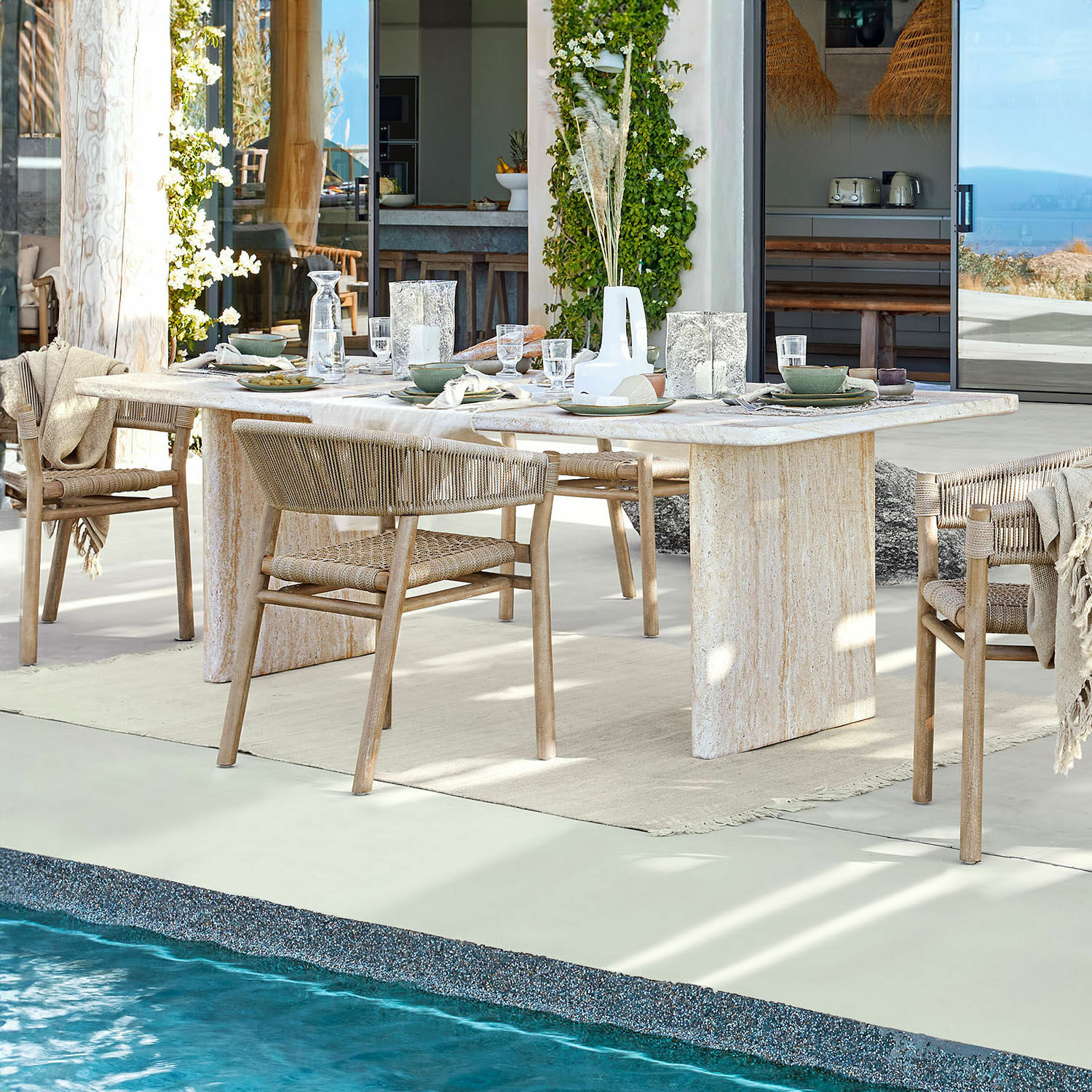 Esstisch Yveline Esstisch aus hellem Stein mit Holzstühlen und geflochtenen Rückenlehnen beim Pool in modernem Haus