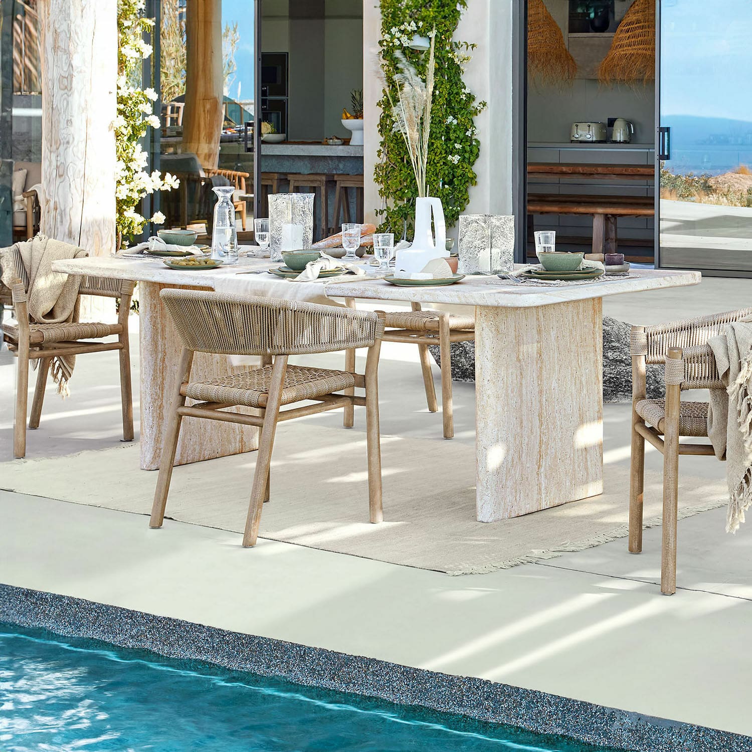 Esstisch Yveline Esstisch aus hellem Stein mit Holzstühlen und geflochtenen Rückenlehnen beim Pool in modernem Haus