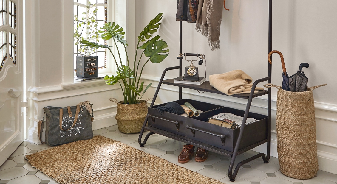 Flur mit schwarzem Metallgarderobenständer, Naturteppich und Korb aus Seegras für Regenschirme und Pflanze