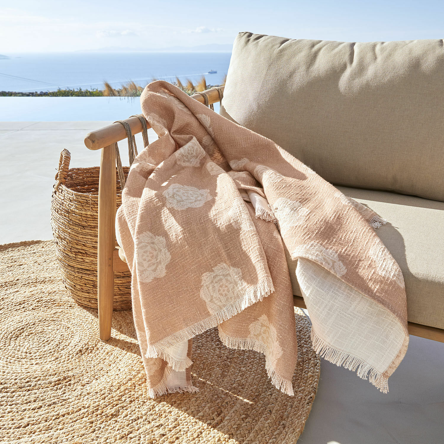 Plaid Belvienne Beige Decke mit weissem Blumenmuster aus weichem Stoff auf Holzstuhl auf Terrasse mit Meerblick
