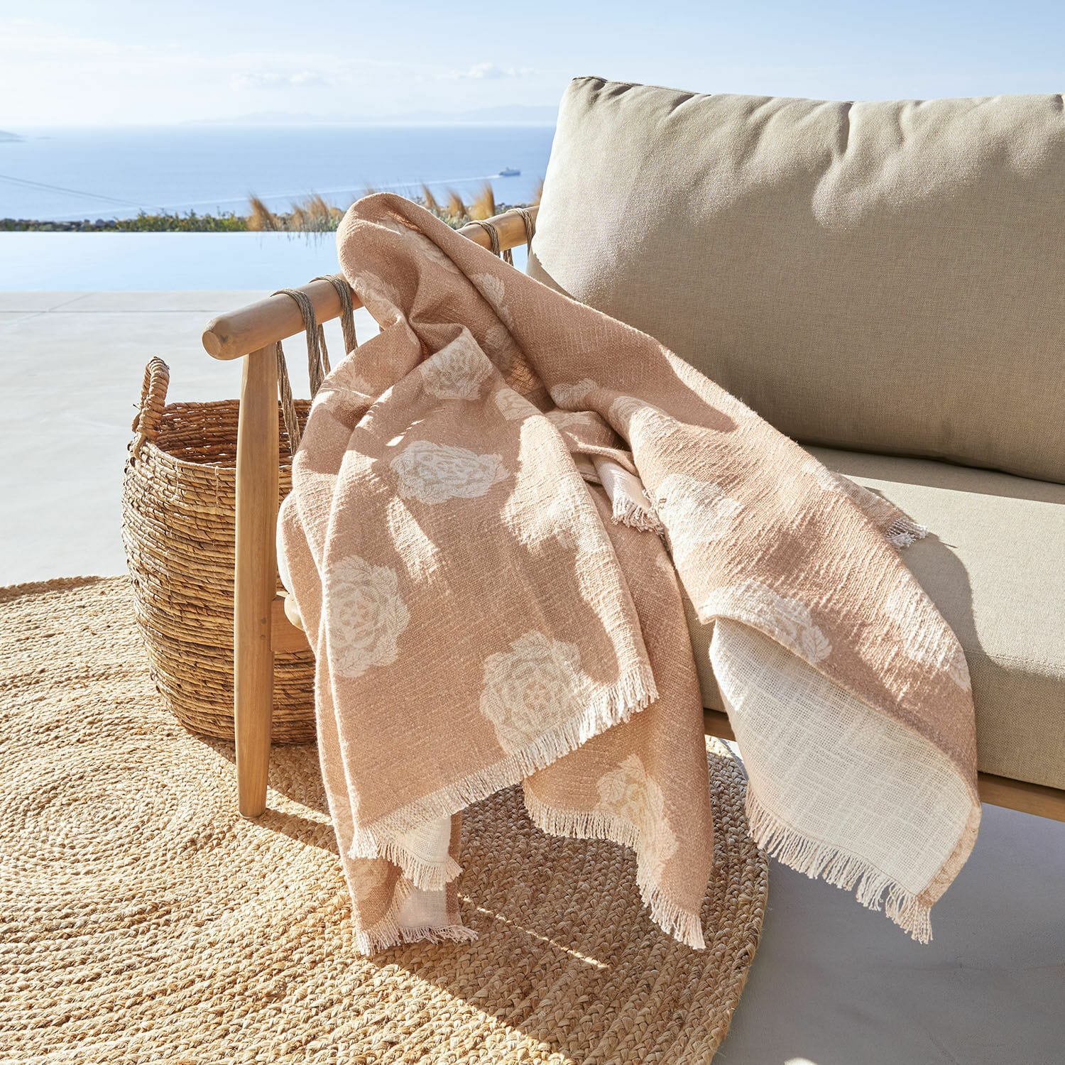 Plaid Belvienne Beige Decke mit weissem Blumenmuster aus weichem Stoff auf Holzstuhl auf Terrasse mit Meerblick