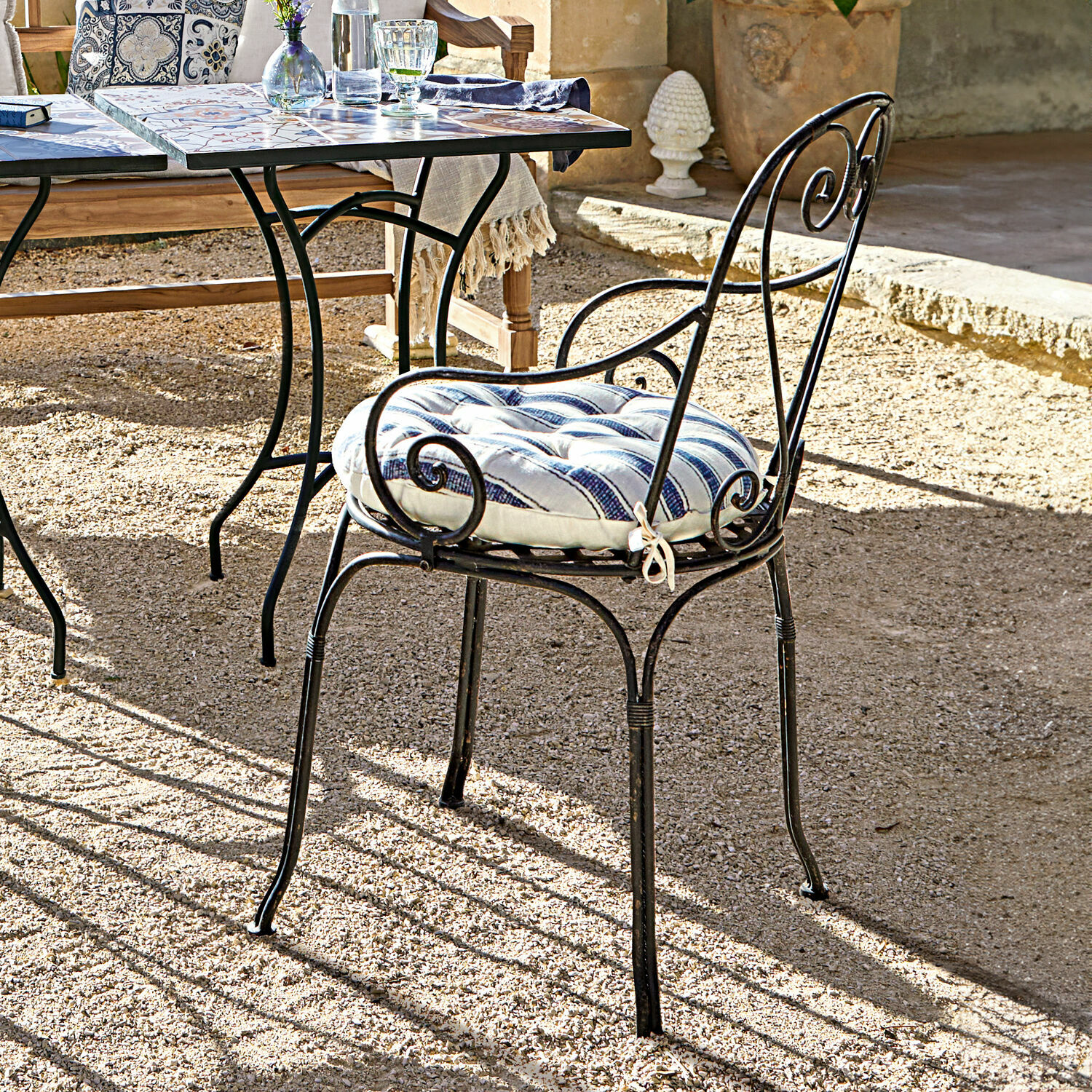 Metall-Gartenstuhl mit blau-weiss gestreiftem Polster auf sonniger Terrasse aus Kies