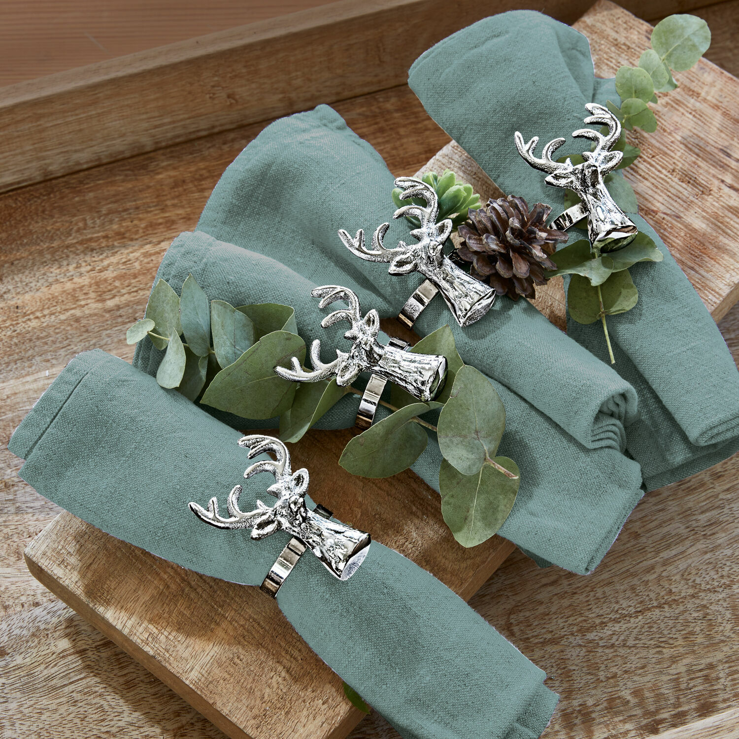 Vier grüne Leinenservietten mit silbernen Serviettenringen in Hirschkopf-Form auf Holztablett