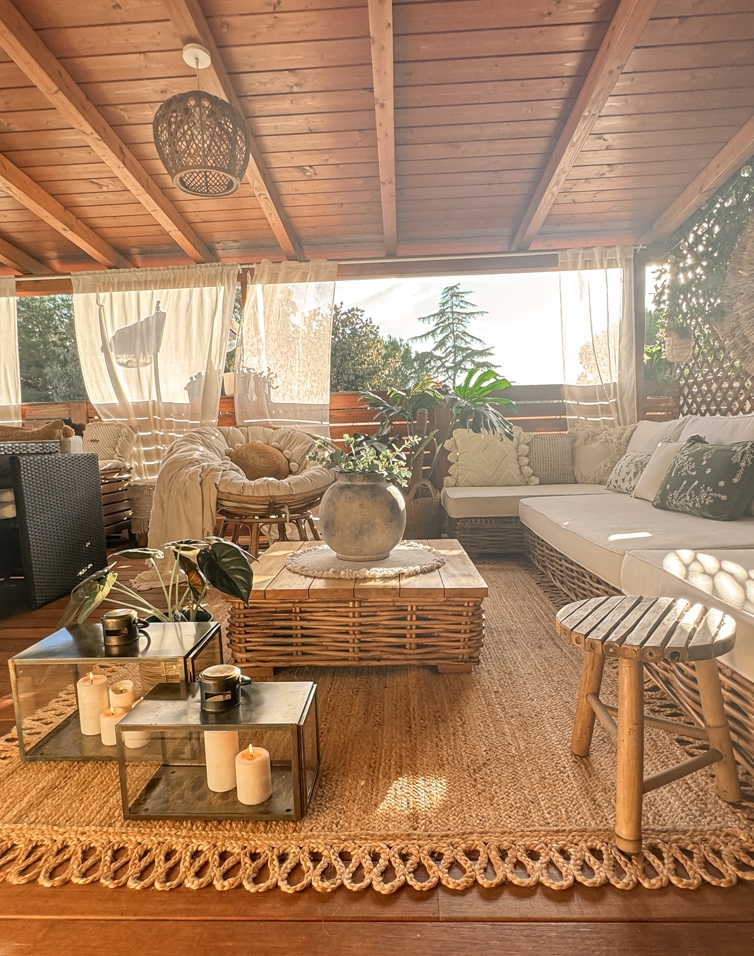 Gemütliche Terrasse mit Rattanmöbeln, Holztisch, Naturstoffen und Pflanzen als Dekoration.