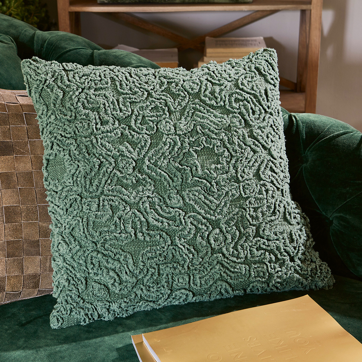 Grünes dekoratives Kissen aus weichem Material auf grünem Sofa, stilvolles Wohnaccessoire