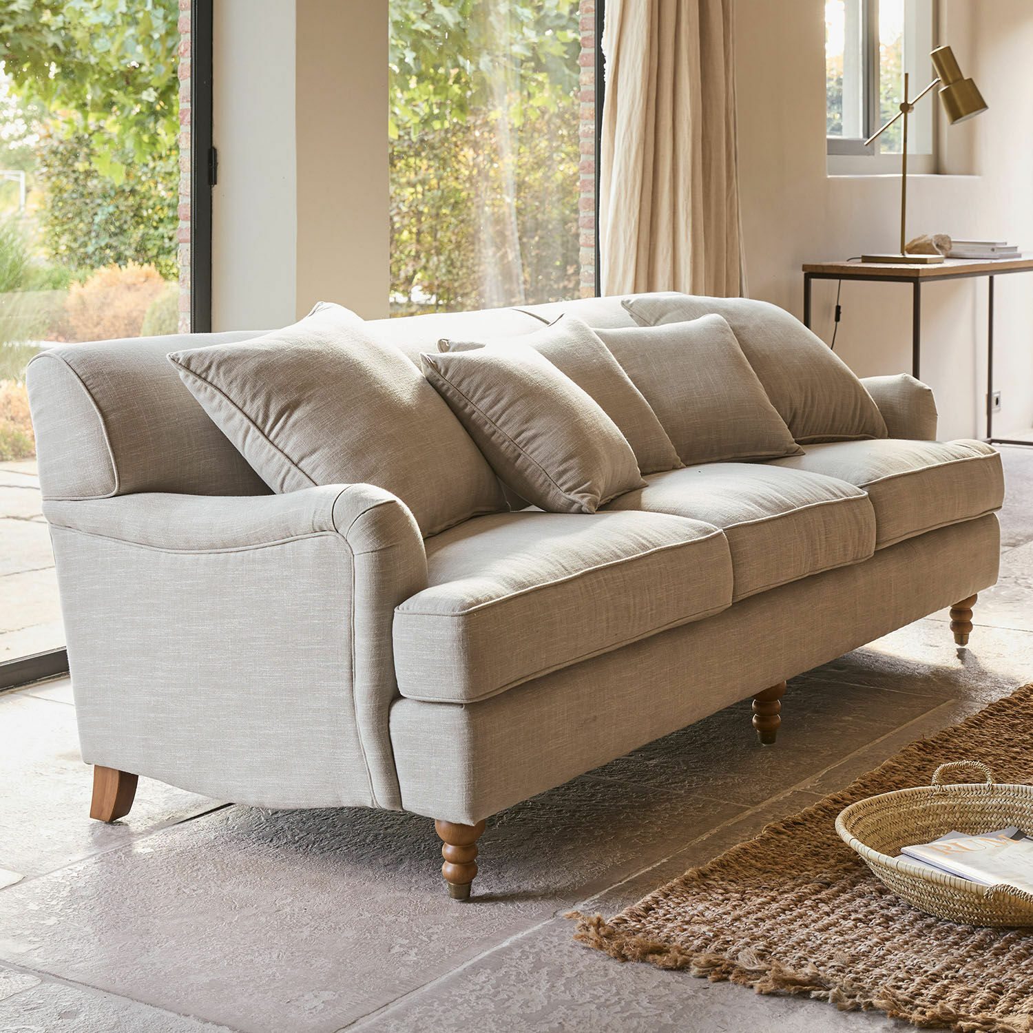 Sofa Isa Sofa mit beigem Bezug, Kissen und Holzfüssen in einem hellen Wohnzimmer mit Teppich