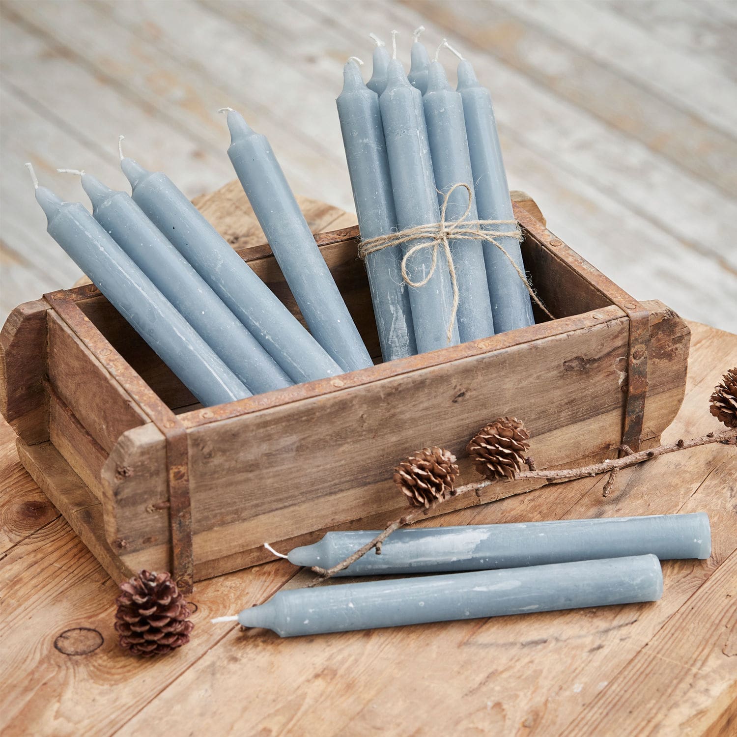 Kerze 12er Set Bauceau Set aus blauen Wachskerzen in Holzkiste auf rustikalem Holztisch mit Kiefernzapfen