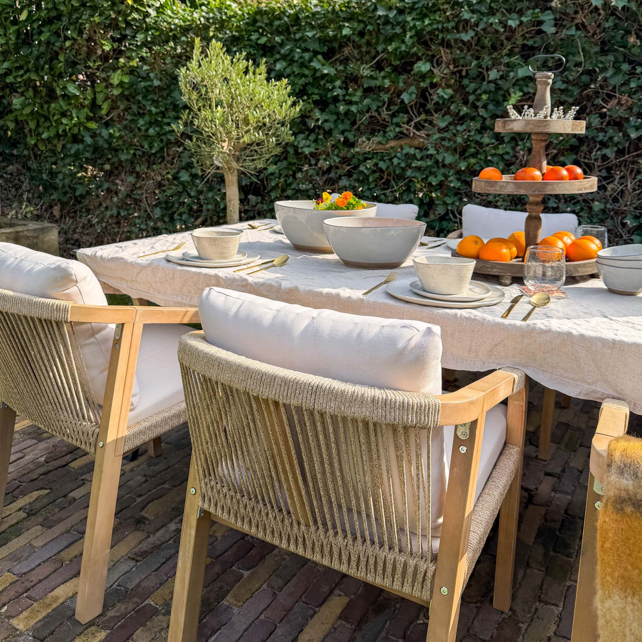 Gartenmöbel-Set mit Holzstühlen und weissen Kissen an gedecktem Tisch mit Geschirr und Obst