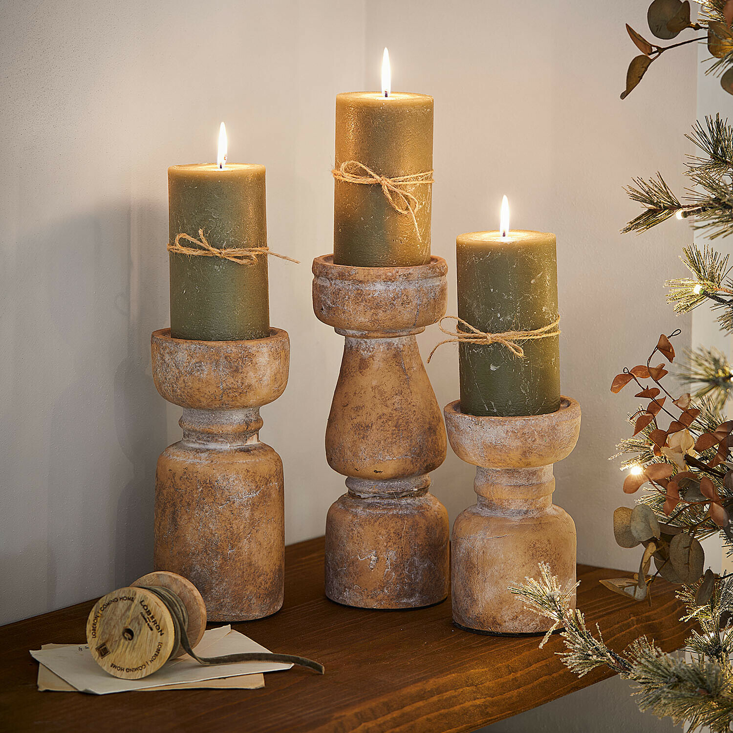 Kerzenständer 3er Set Talona Drei rustikale Holzkerzenhalter mit grünen Kerzen und Juteschnur auf dekorativem Holzregal