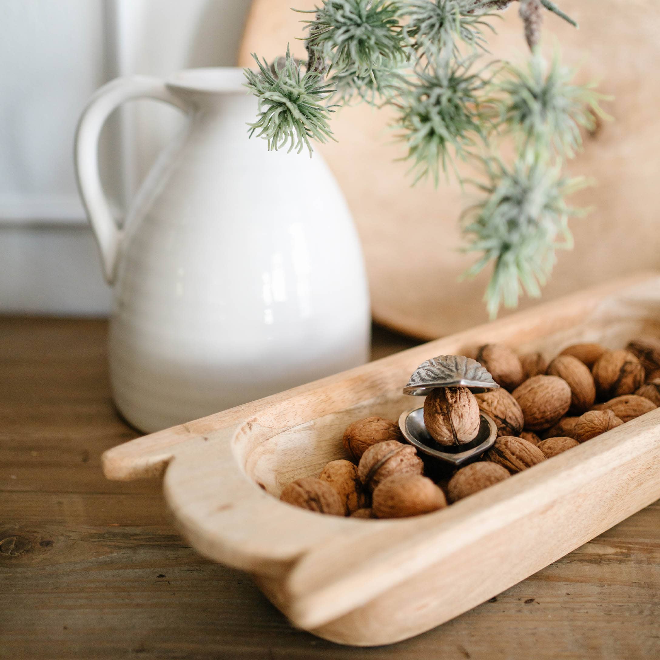 Holztablett mit Walnüssen und Metallnussknacker auf Holztisch neben weissem Krug