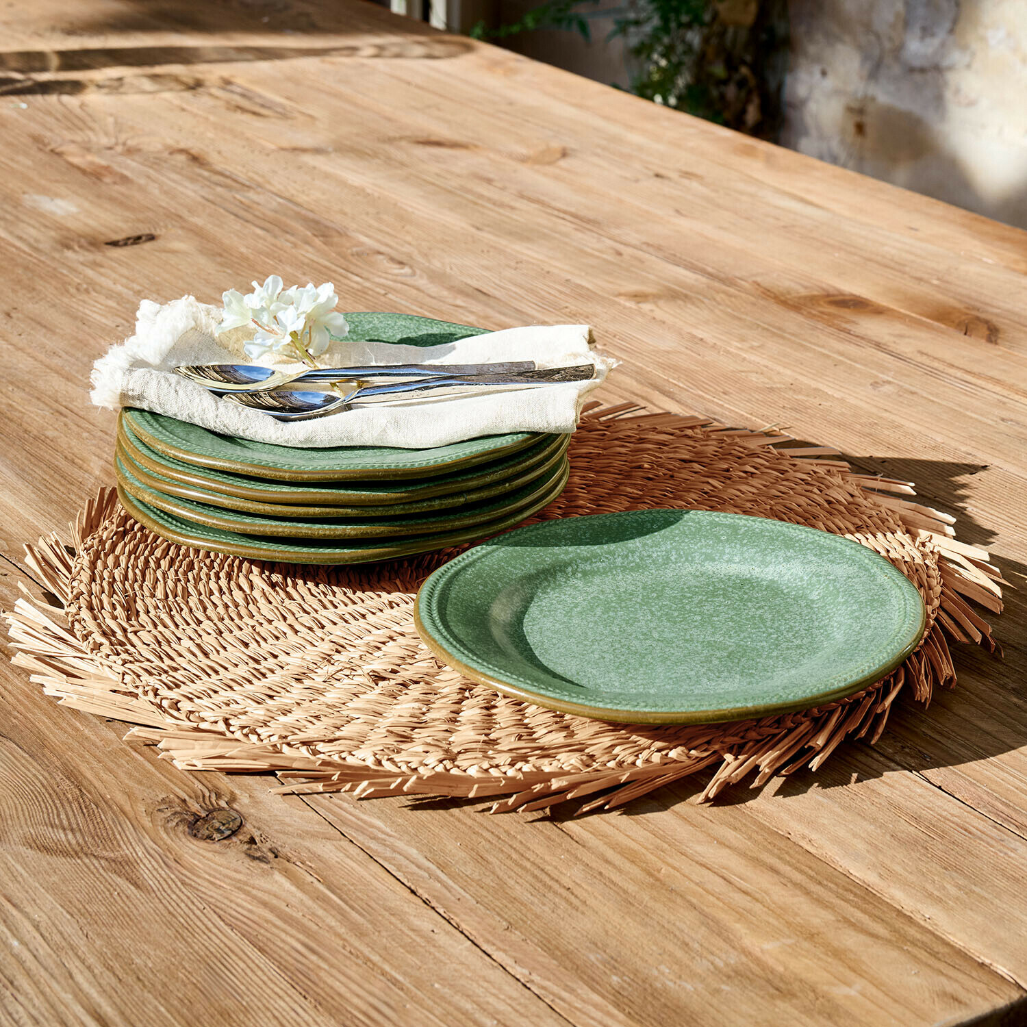 Grünes Keramik-Teller-Set auf geflochtenem Untersetzer auf Holztisch mit Metallbesteck