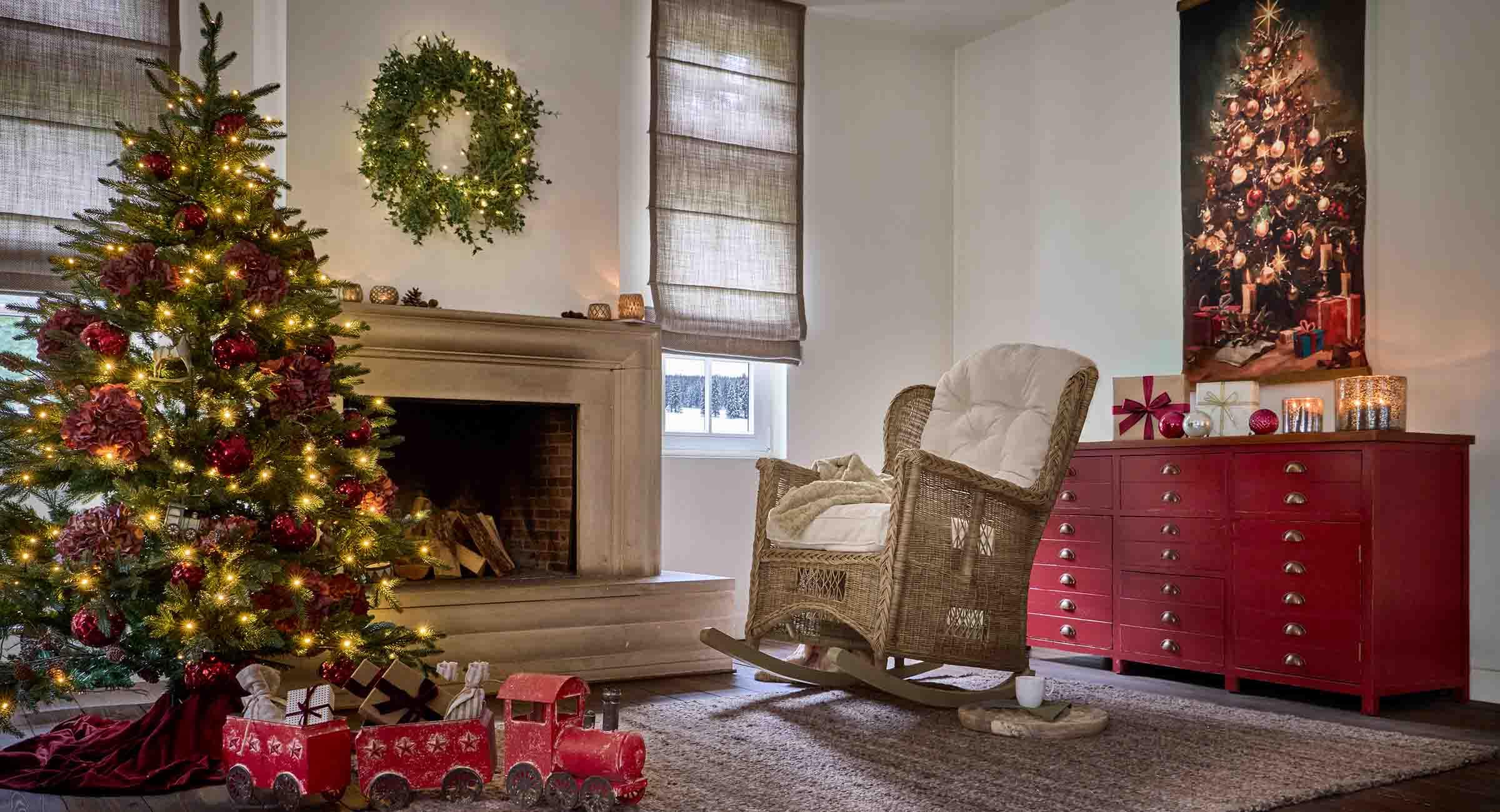 Gemütliches Wohnzimmer mit Weihnachtsbaum, Rattansessel und rotem Sideboard festlich dekoriert