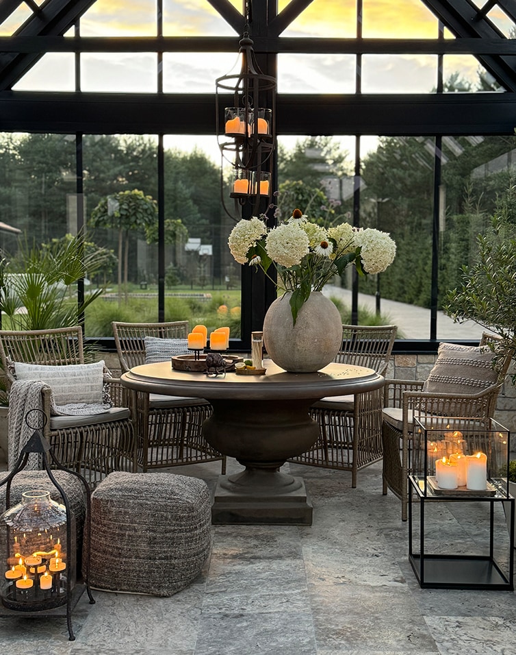Gemütlicher Wintergarten mit rundem Tisch, Rattanstühlen und Kerzenlichtdekoration auf Steinboden