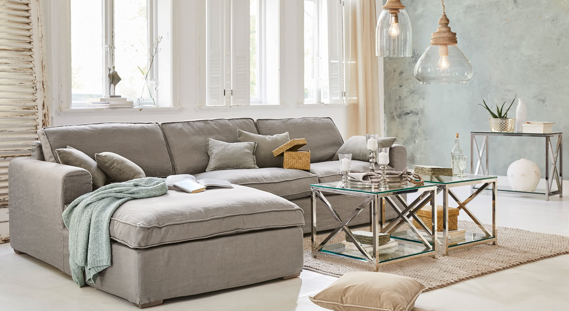 Graues Ecksofa aus Stoff im hellen Wohnzimmer mit Metall-Couchtischen und Dekorationen