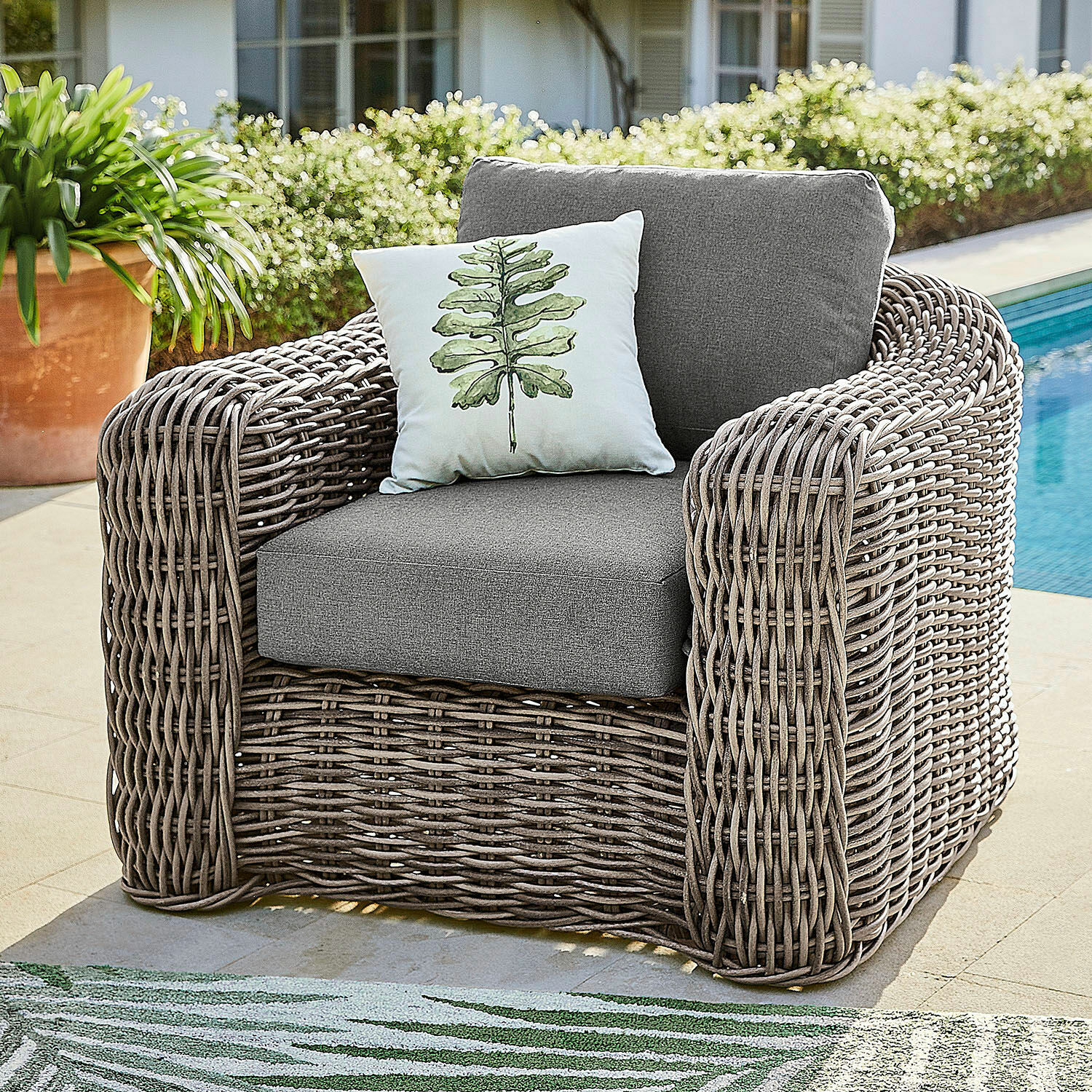 Sessel Upminster Grau geflochtener Gartensessel mit grauen Polstern und dekorativem Blattkissen am Pool