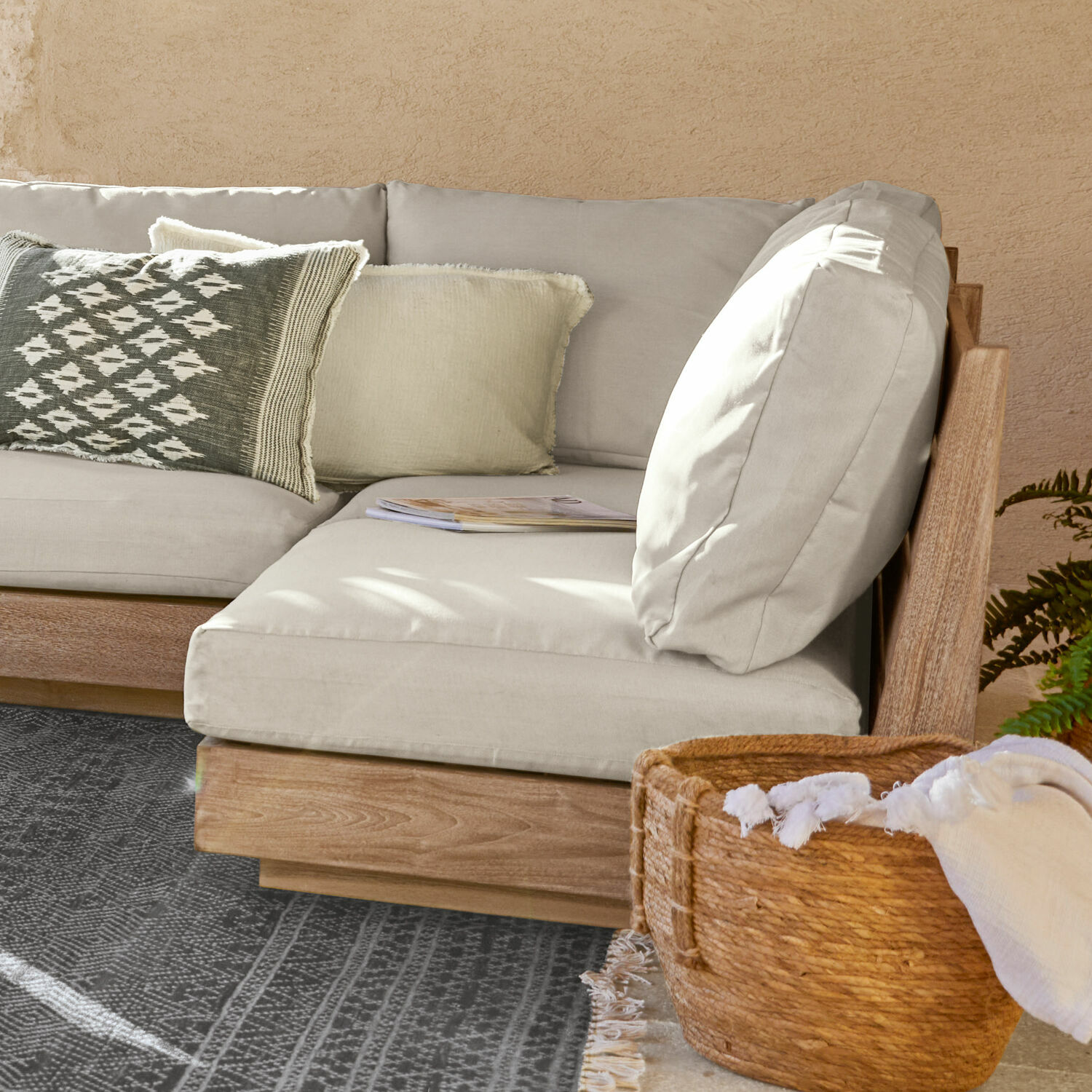 Ecksofa mit hellgrauem Stoffbezug und Holzrahmen, dekorativem Kissen und Korb mit Stoffdecke