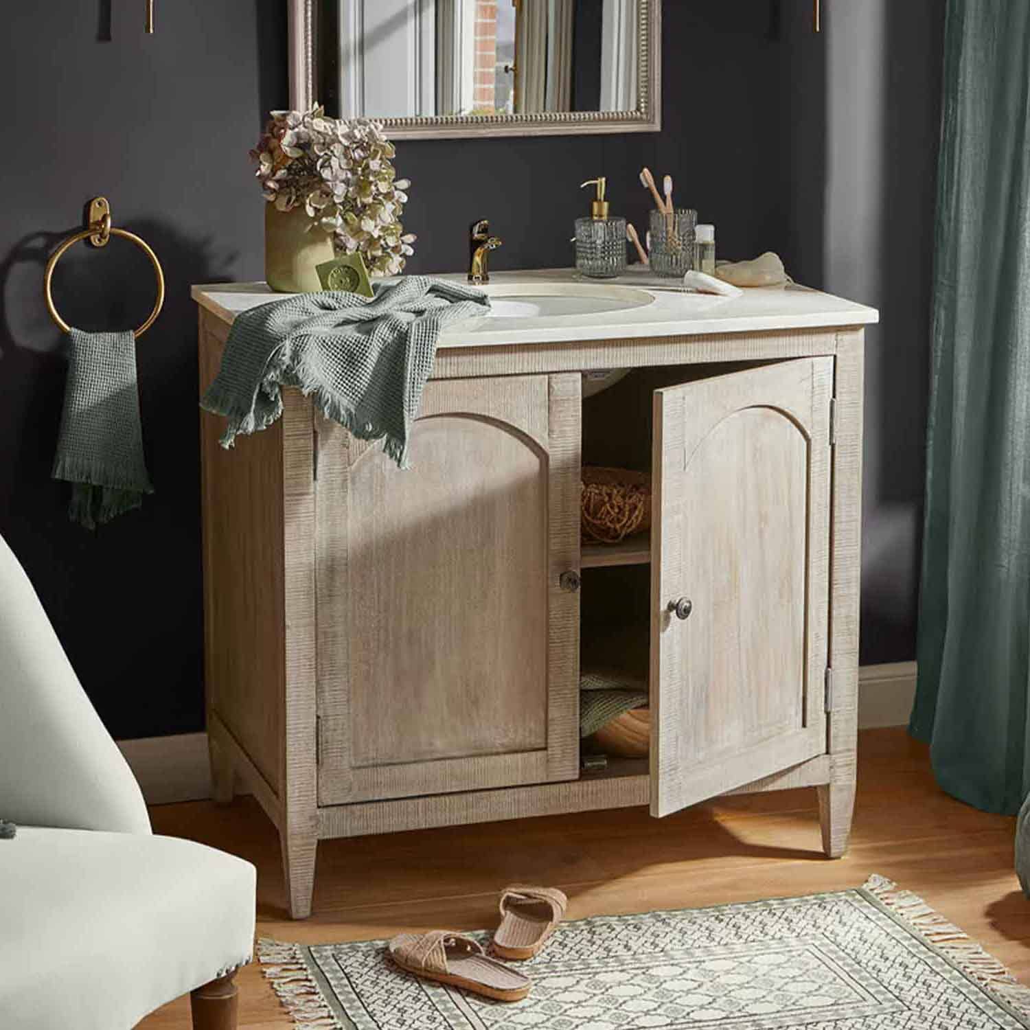 Helles Holz-Badezimmermöbel mit weissem Waschbecken und goldener Armatur, grüne Handtücher und Dekoration