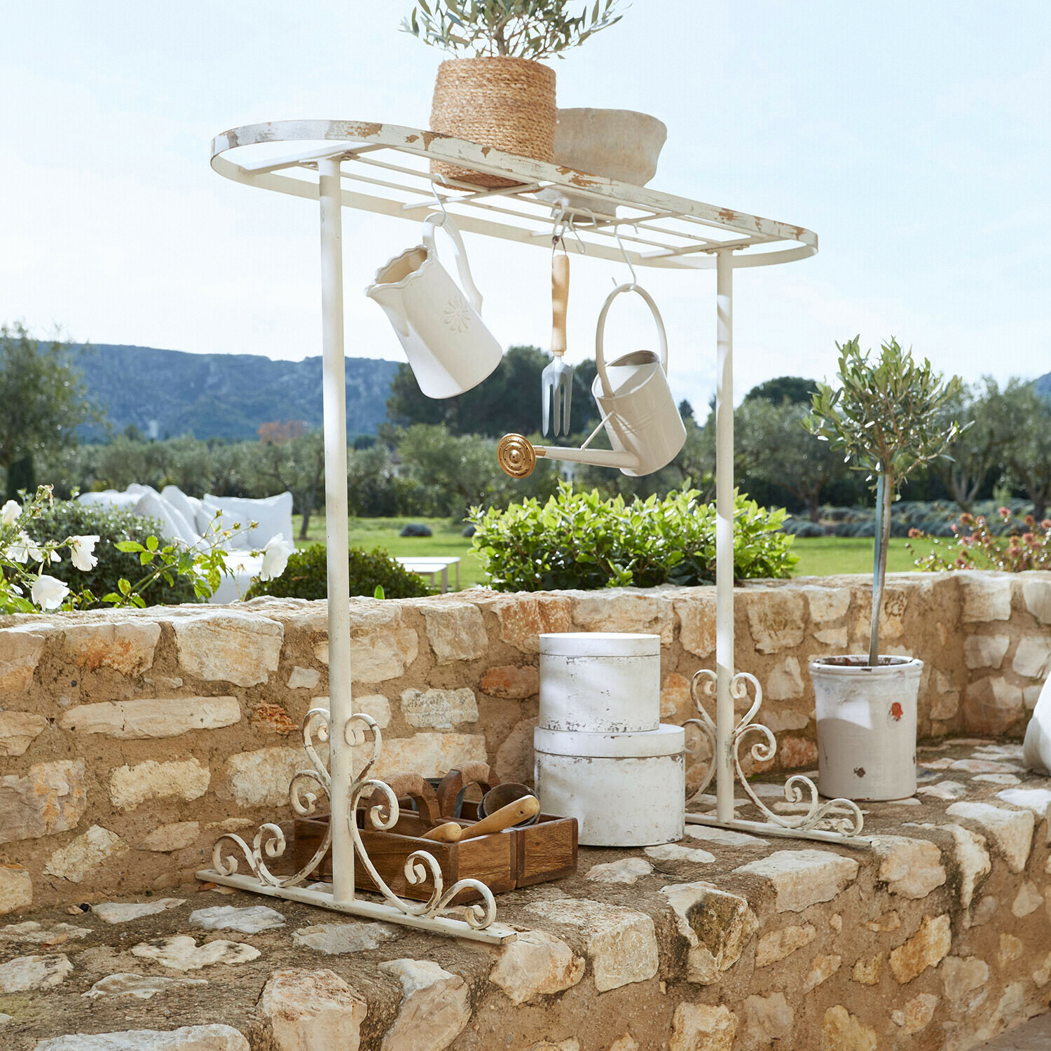 Weisse Metall-Gartenablage mit hängenden Accessoires und Blumentopf auf Steinmauer im Garten