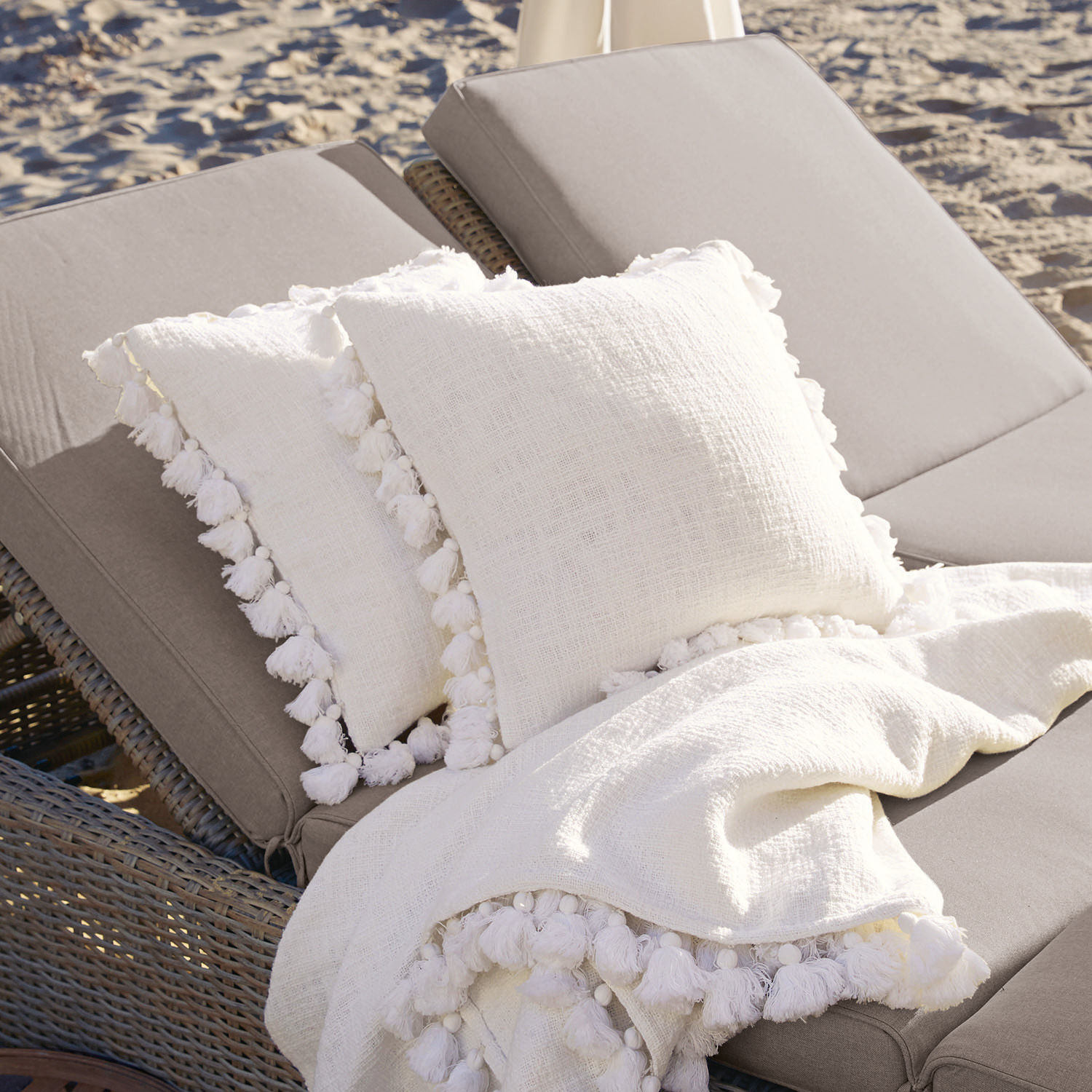 Kissenhülle 2er Set Peniel Weisse Leinenkissen und Decke mit Quasten auf grauem Gartenliegestuhl am Strand