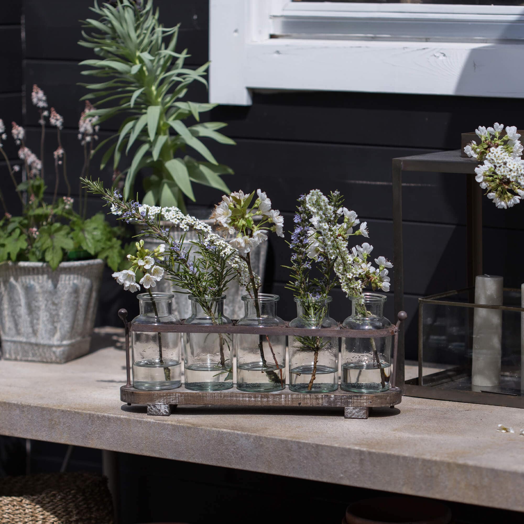 Glasflaschen mit weissen Blumen in Metallhalter auf Steintisch, dekorative Gartendekoration