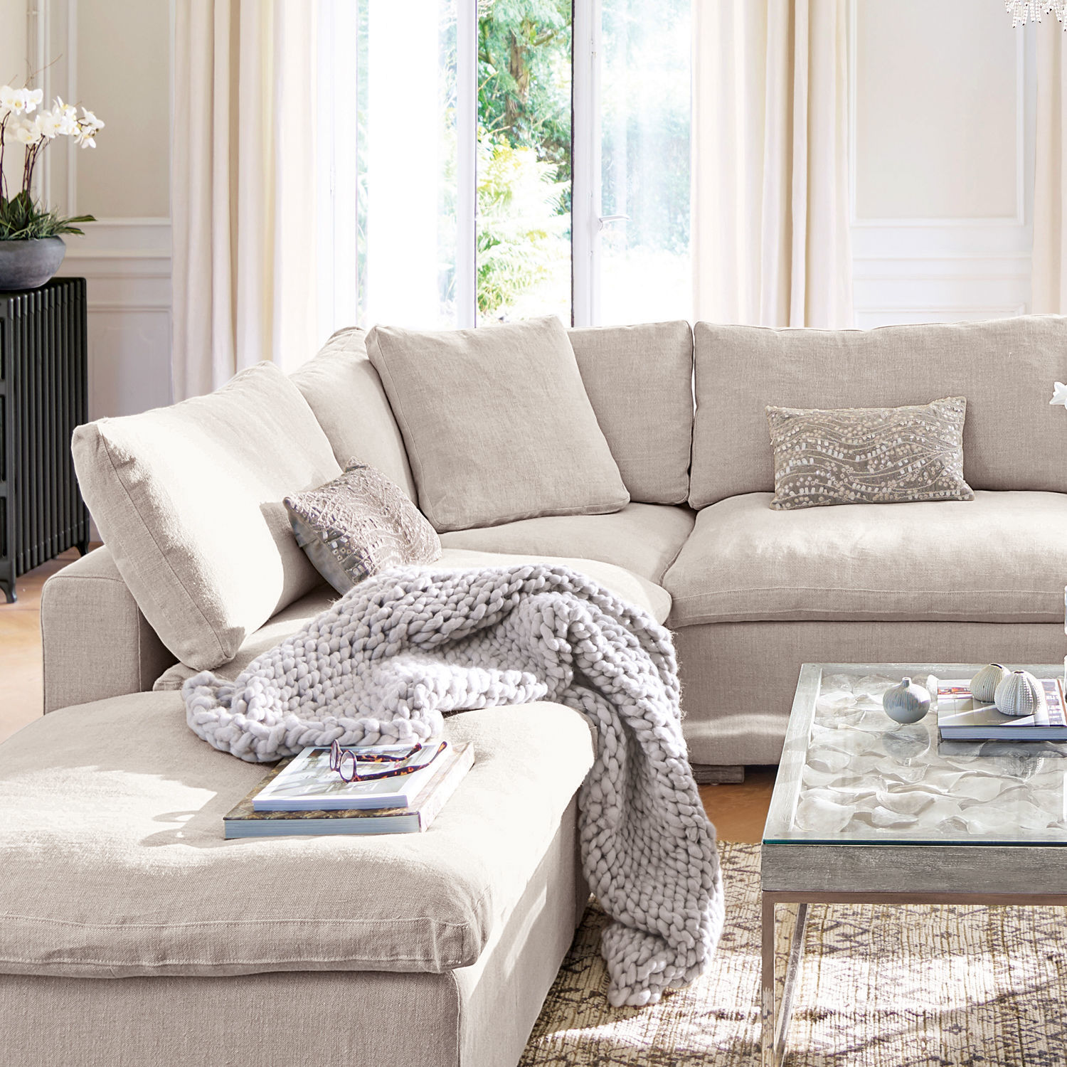 Sessel Bennington Corner Beiges Ecksofa aus Stoff mit Kissen und grauer Strickdecke in hellem Wohnzimmer