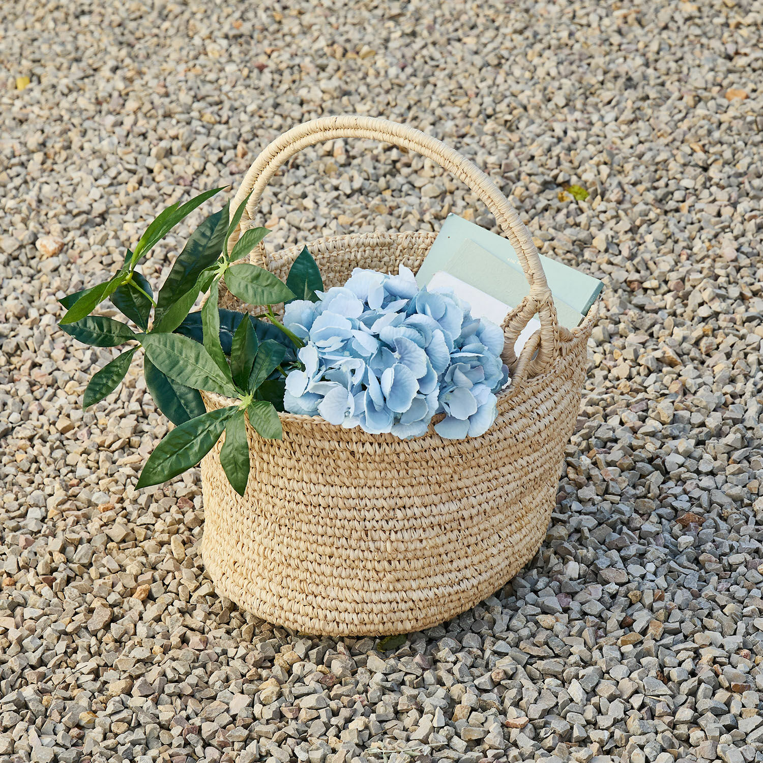 Korb Shanoura Naturfarbener Korb aus Seegras mit blauen Blumen und grünen Blättern auf Kieselsteinen