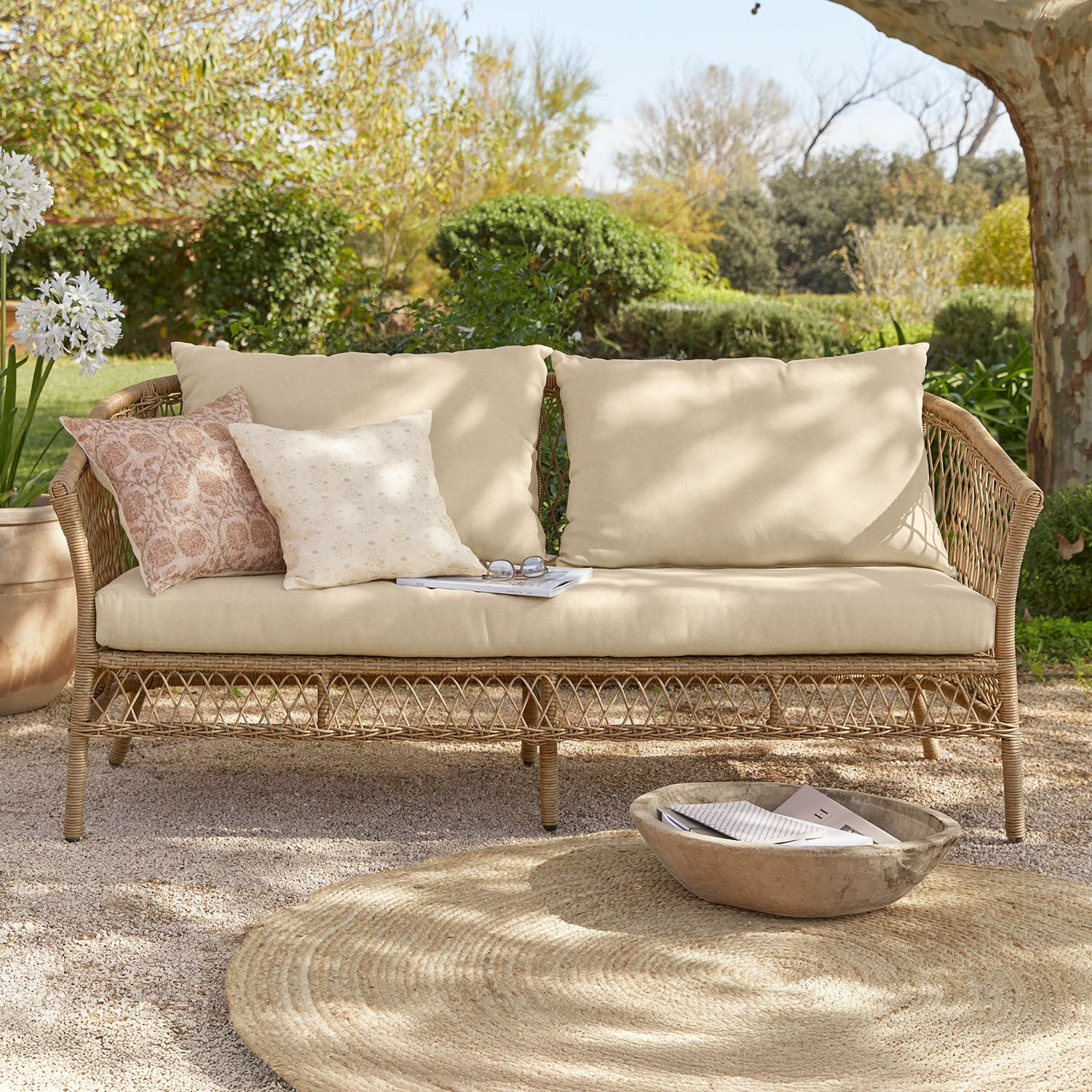 Sofa Farington Rattansofa mit beigen Polstern und pastellfarbenen Zierkissen in sonnigem Gartensitzplatz