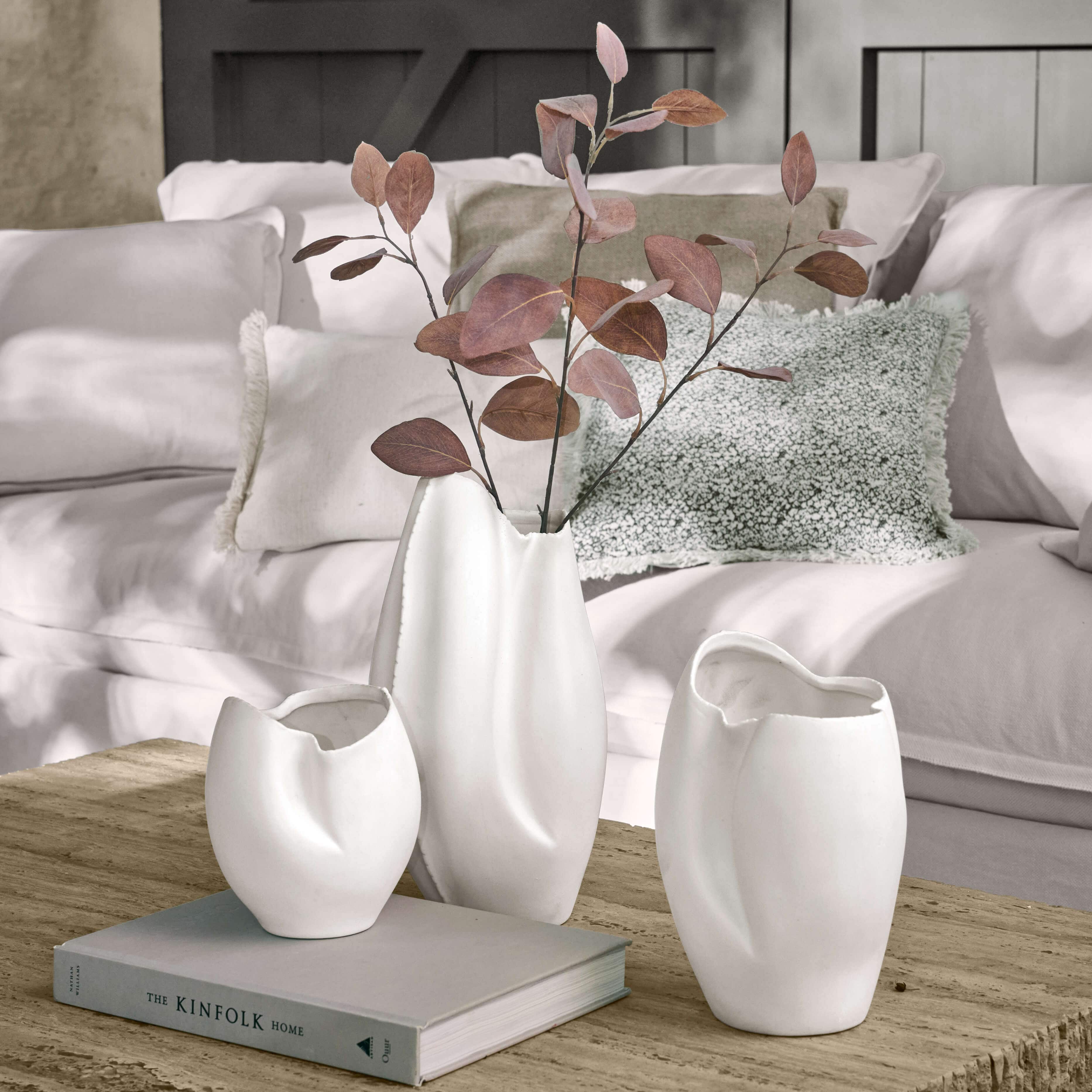 Set mit drei weissen Keramikvasen mit unregelmässiger Form auf Holztisch im Wohnzimmer