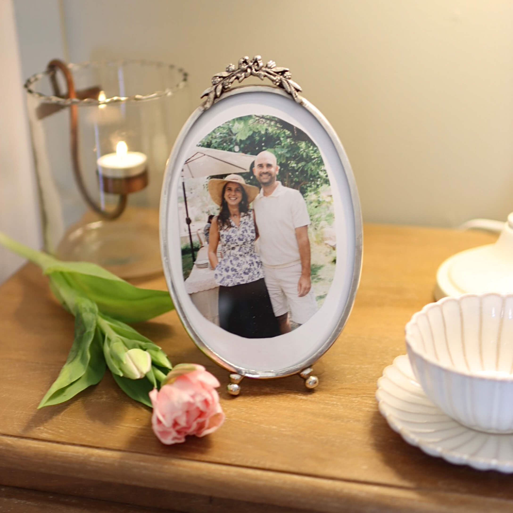 Ovale silberne Bilderrahmen mit floralem Dekor auf Holztisch mit Rose und Kerzenhalter