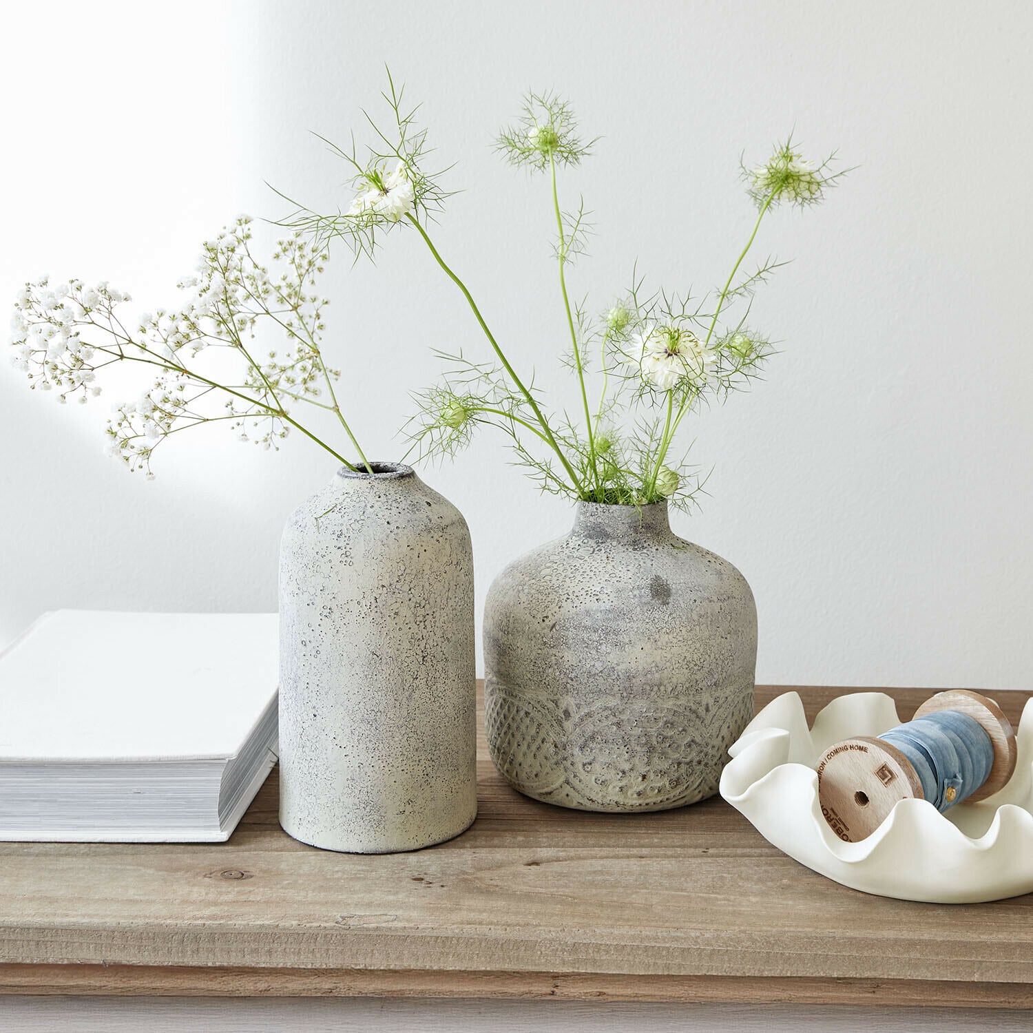 Zwei graue Keramikvasen mit zarten weissen Blumen auf hellem Holztisch dekorativ arrangiert