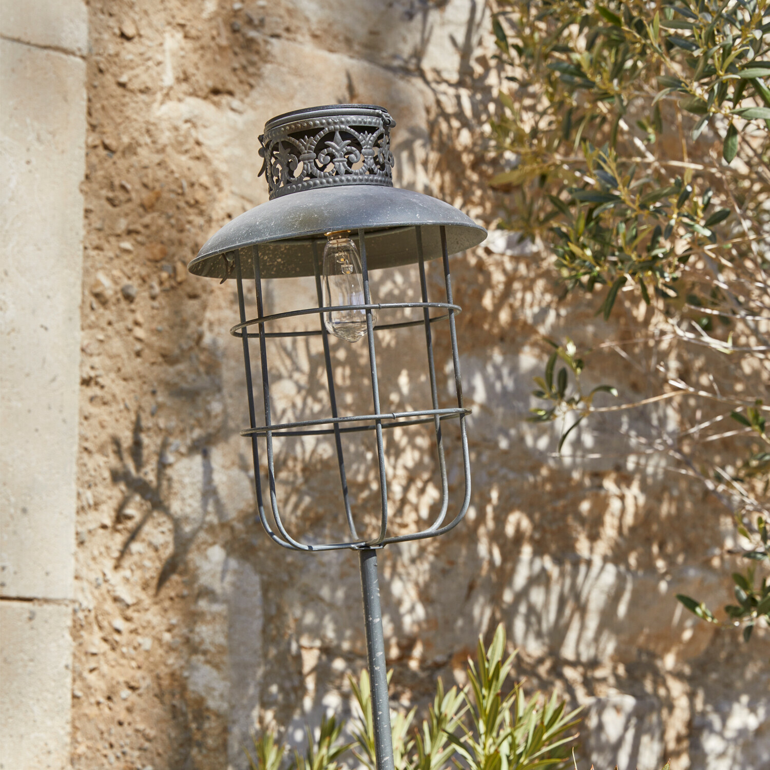Solar-Laterne Nistos Metall-Gartenlampe im Vintage-Stil mit schwarzem Schirm und dekorativem Muster vor Steinmauer