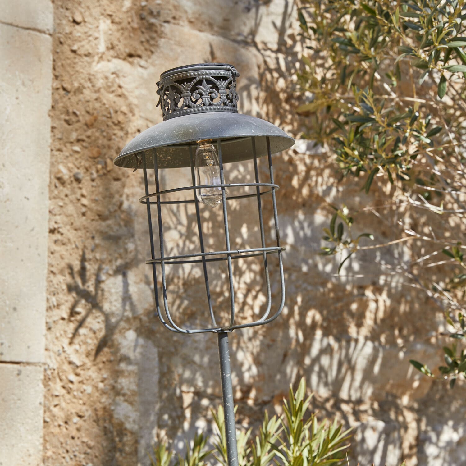 Solar-Laterne Nistos Metall-Gartenlampe im Vintage-Stil mit schwarzem Schirm und dekorativem Muster vor Steinmauer