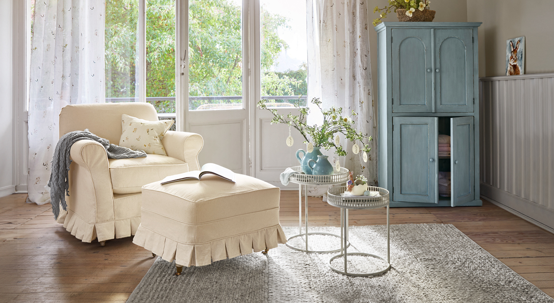 Beiger Stoffsessel mit Hocker im nostalgischen Stil in hellem Wohnzimmer mit blauem Schrank