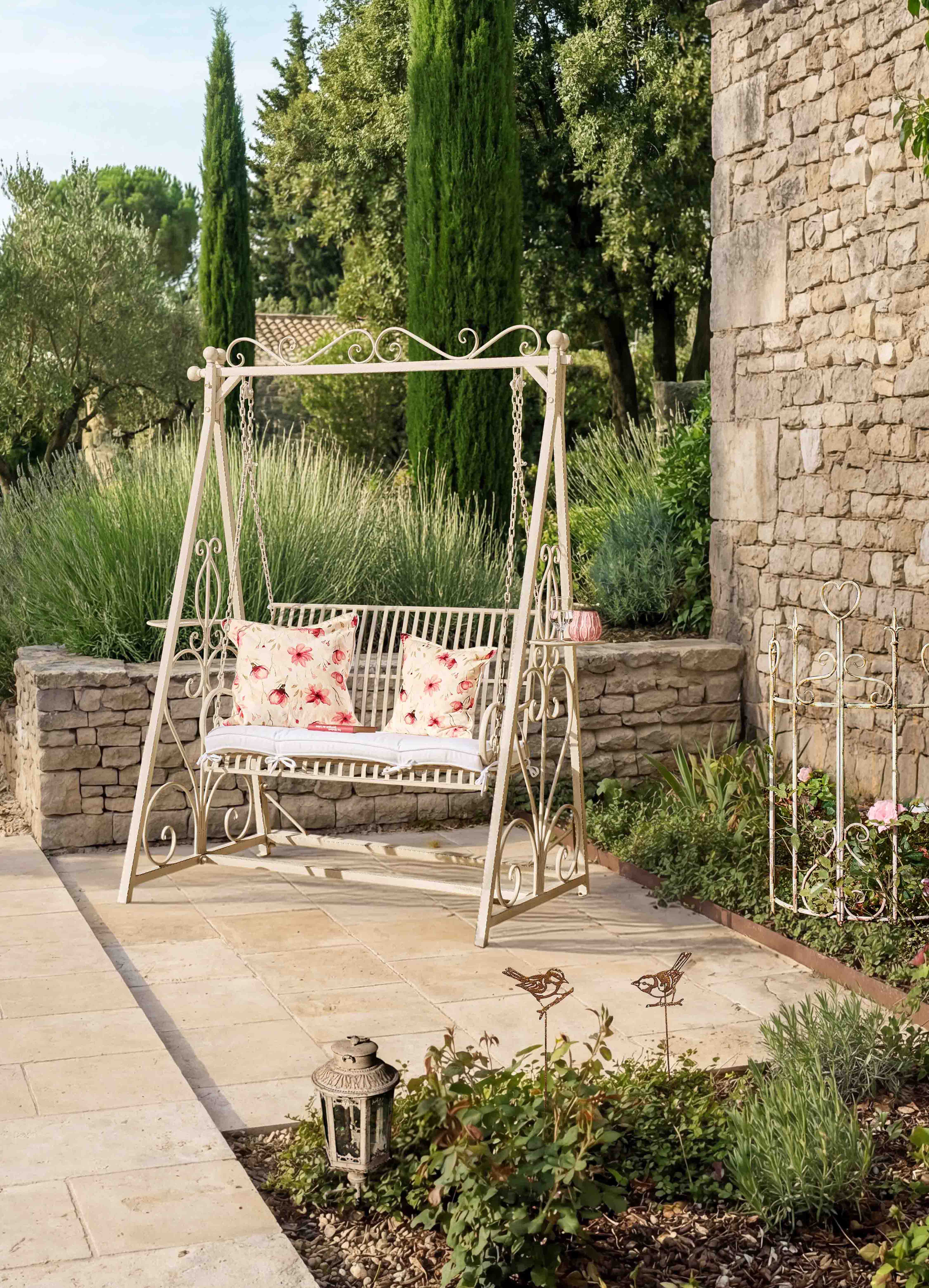 Metall-Gartenschaukel in Creme mit floralen Kissen auf Terrasse mit Natursteinmauer