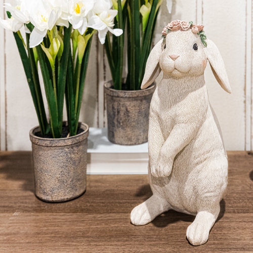 Dekorativer weisser Hase mit Blumenkranz auf Holztisch neben Töpfen mit weissen Blumen
