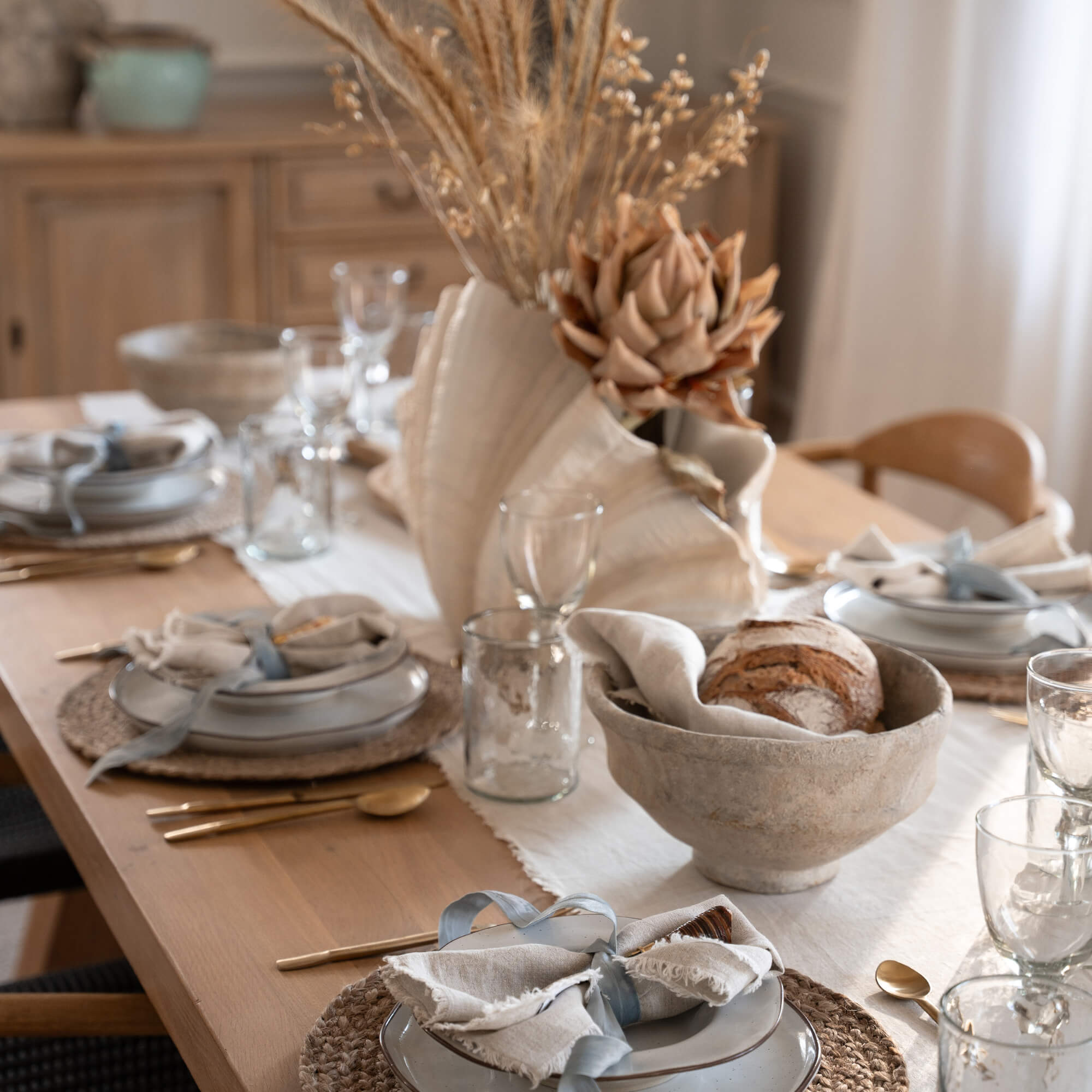 Rustikaler Holztisch mit natürlichem Läufer, Keramiktellern und getrockneten Blumen als Dekoration.