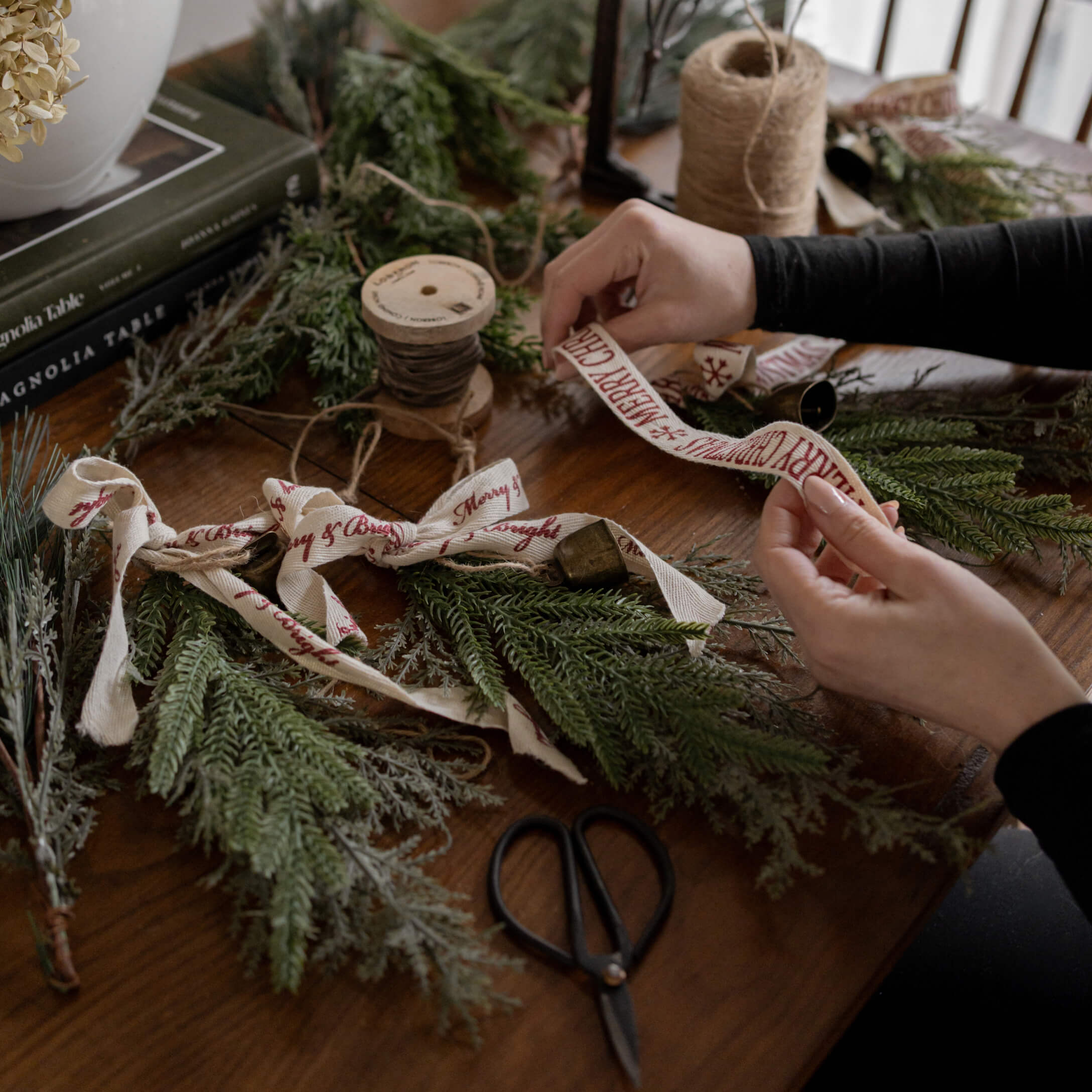 Hände binden grüne Tannenzweige mit Baumwollband Merry Christmas auf Holztisch mit Schere