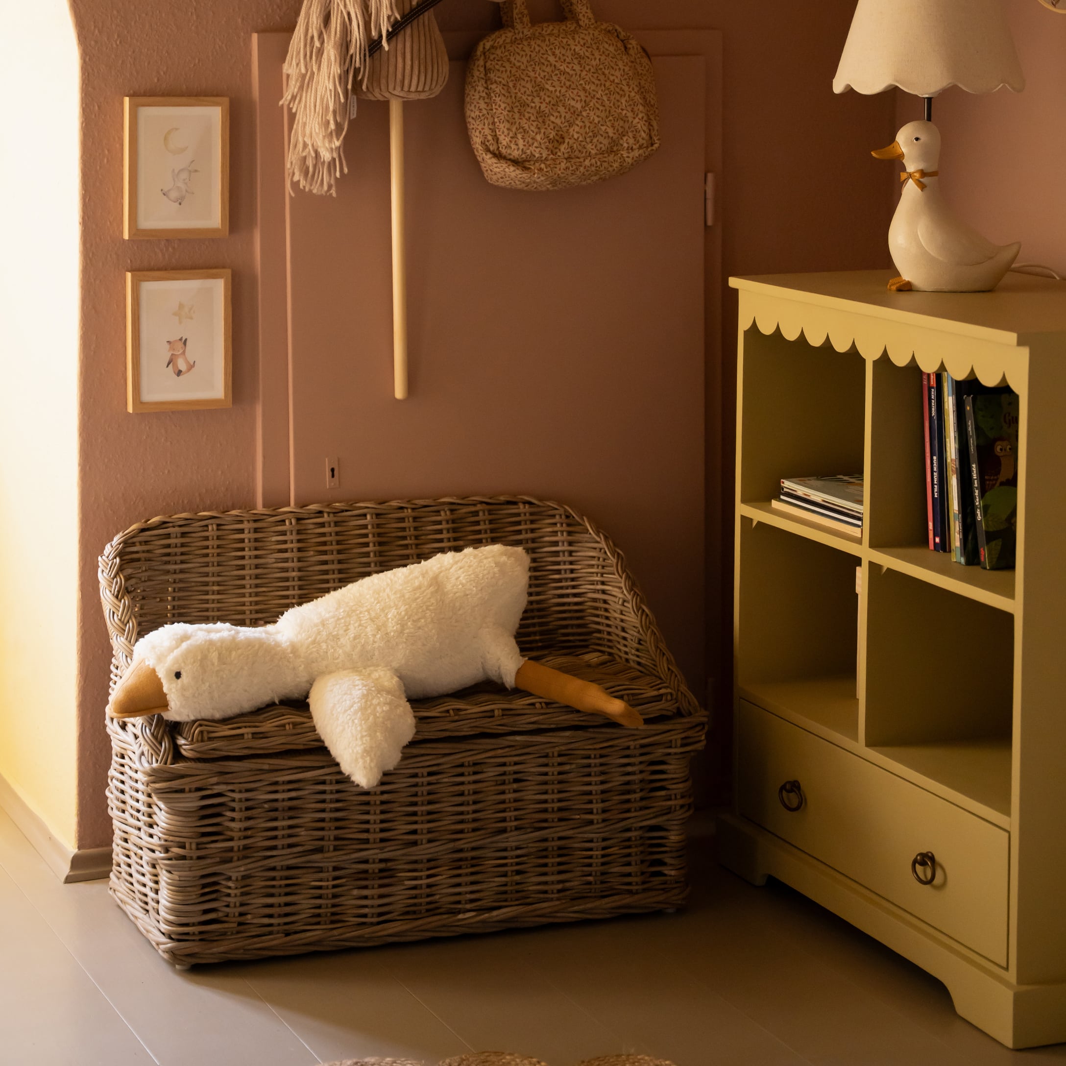 Weidenbank mit langem weissem Plüsch-Entenkissen in gemütlichem Kinderzimmer mit gelbem Regal