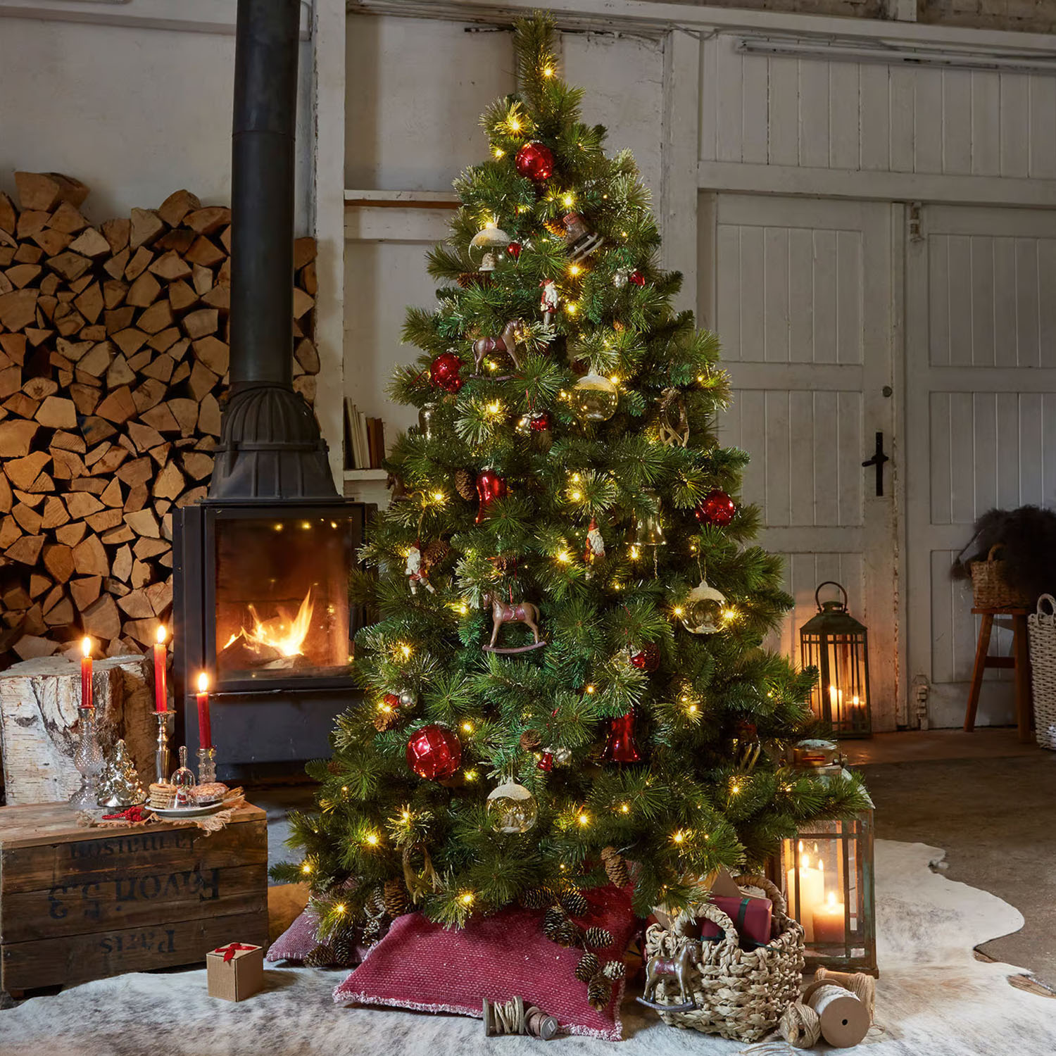 Geschmückter grüner Weihnachtsbaum mit roten und goldenen Kugeln und Lichterketten in gemütlichem Raum mit Kamin
