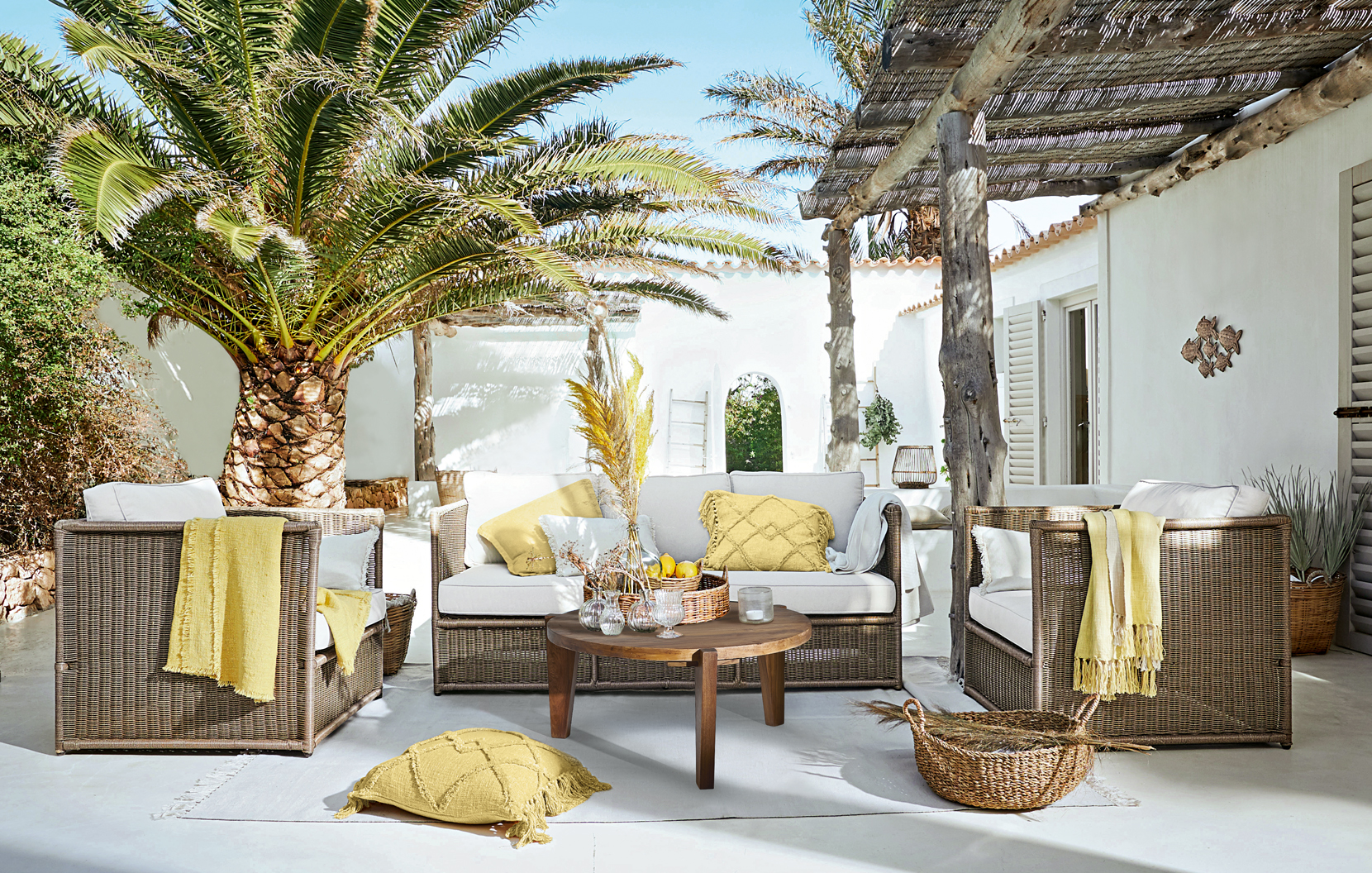 Braunes Rattan-Gartenmöbel-Set mit cremefarbenen Polstern und gelben Akzenten auf sonniger Terrasse