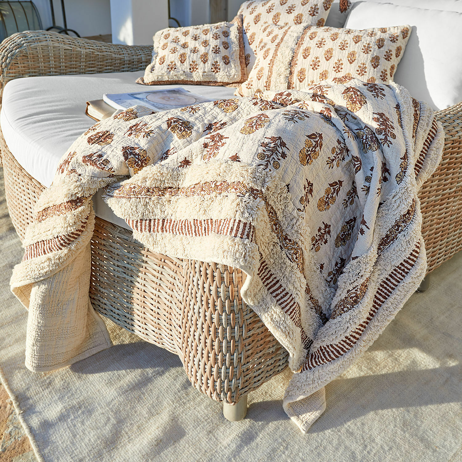 Plaid Arsalan Beige Baumwolldecke und Kissen mit braunem Muster auf Rattansofa auf der Terrasse