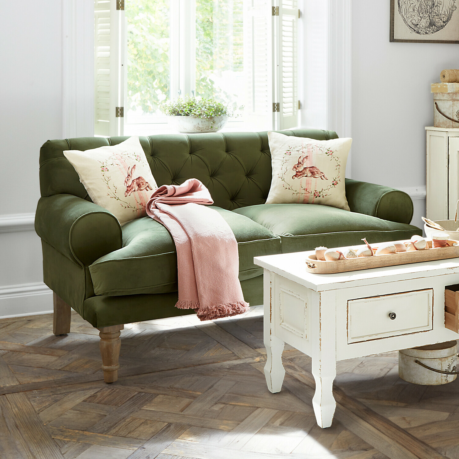 Sofa Carme Grünes Samtsofa mit Hasen-Kissen und rosa Decke in hellem Wohnzimmer
