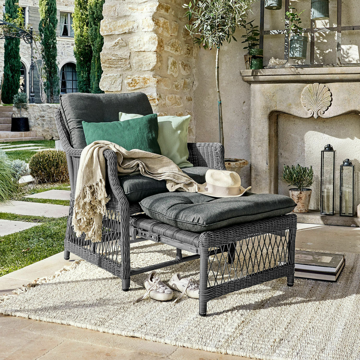 Sessel Howe Grauer Rattansessel mit Fusshocker und dunkelgrauen Kissen, dekoriert mit grünen Kissen auf der Terrasse