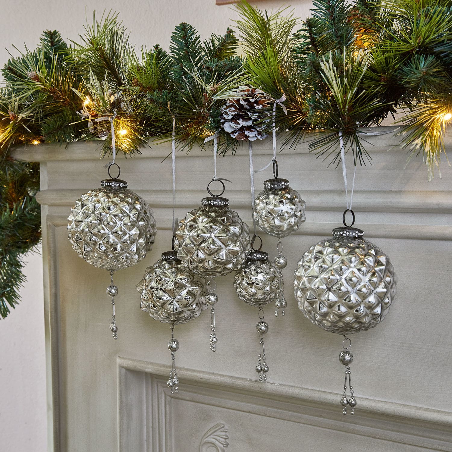 Weihnachtsschmuck 6er Set Murron Silberne Glas-Weihnachtskugeln mit Anhängern vor dem Kamin und grünen Zweigen mit Lichterkette