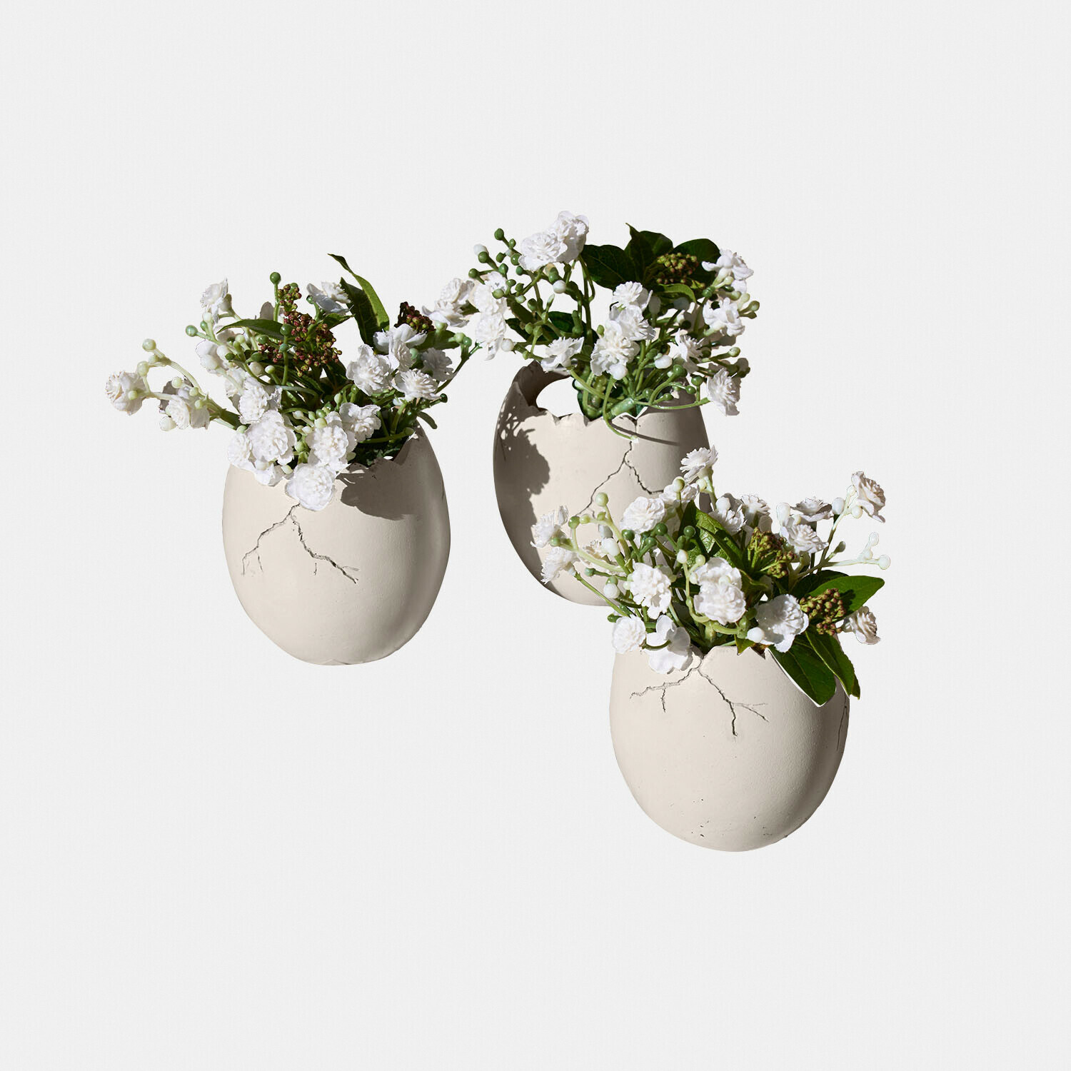 Deko-Ei 3er Set Waverlye Drei weisse Keramikvasen in Ei-Form mit weissen Blumen und grünen Blättern als Dekoration.