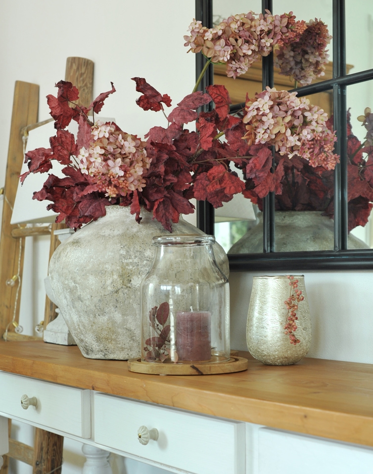 Dekorative Steinvase mit roten Blättern und rosa Blüten auf Holztisch im Wohnzimmer