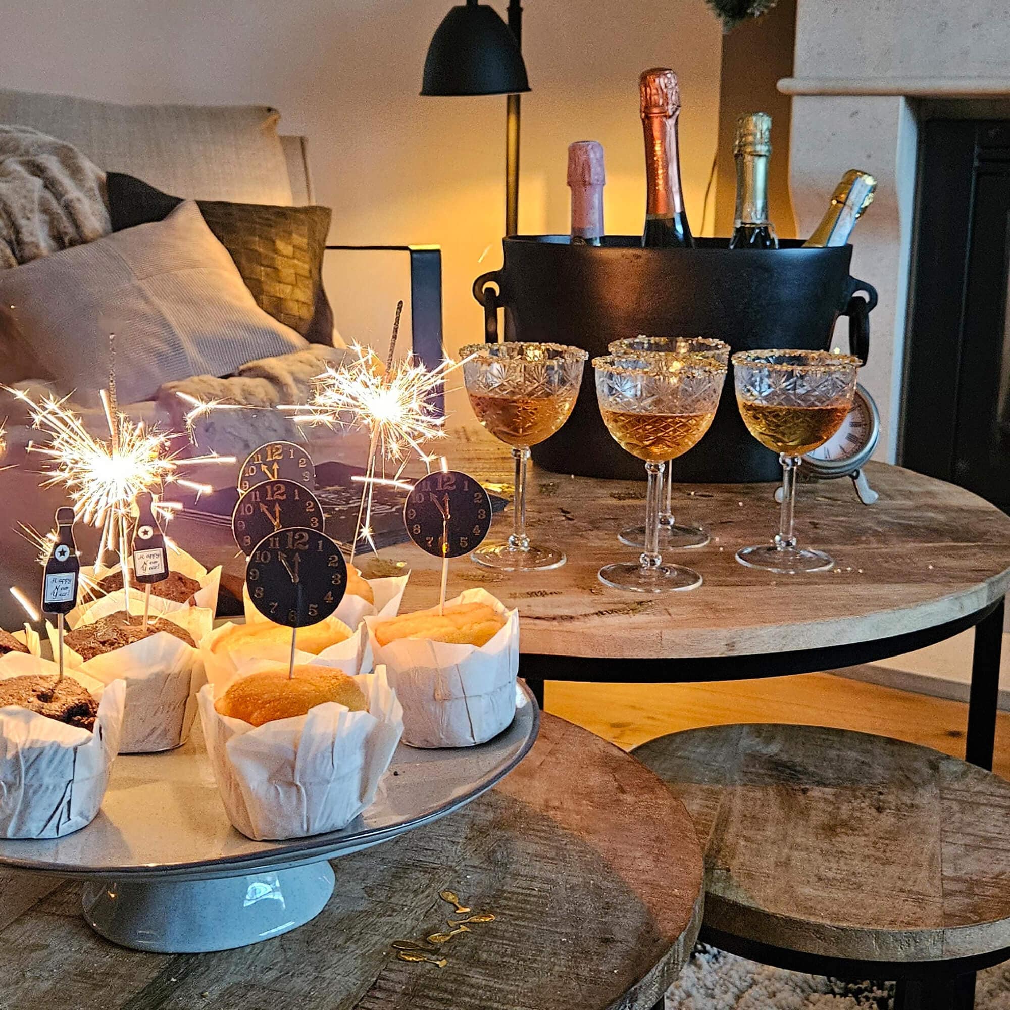 Feiere mit Muffins, Gläsern und Flaschen im Eimer auf einem Holztisch in einem gemütlichen Raum.
