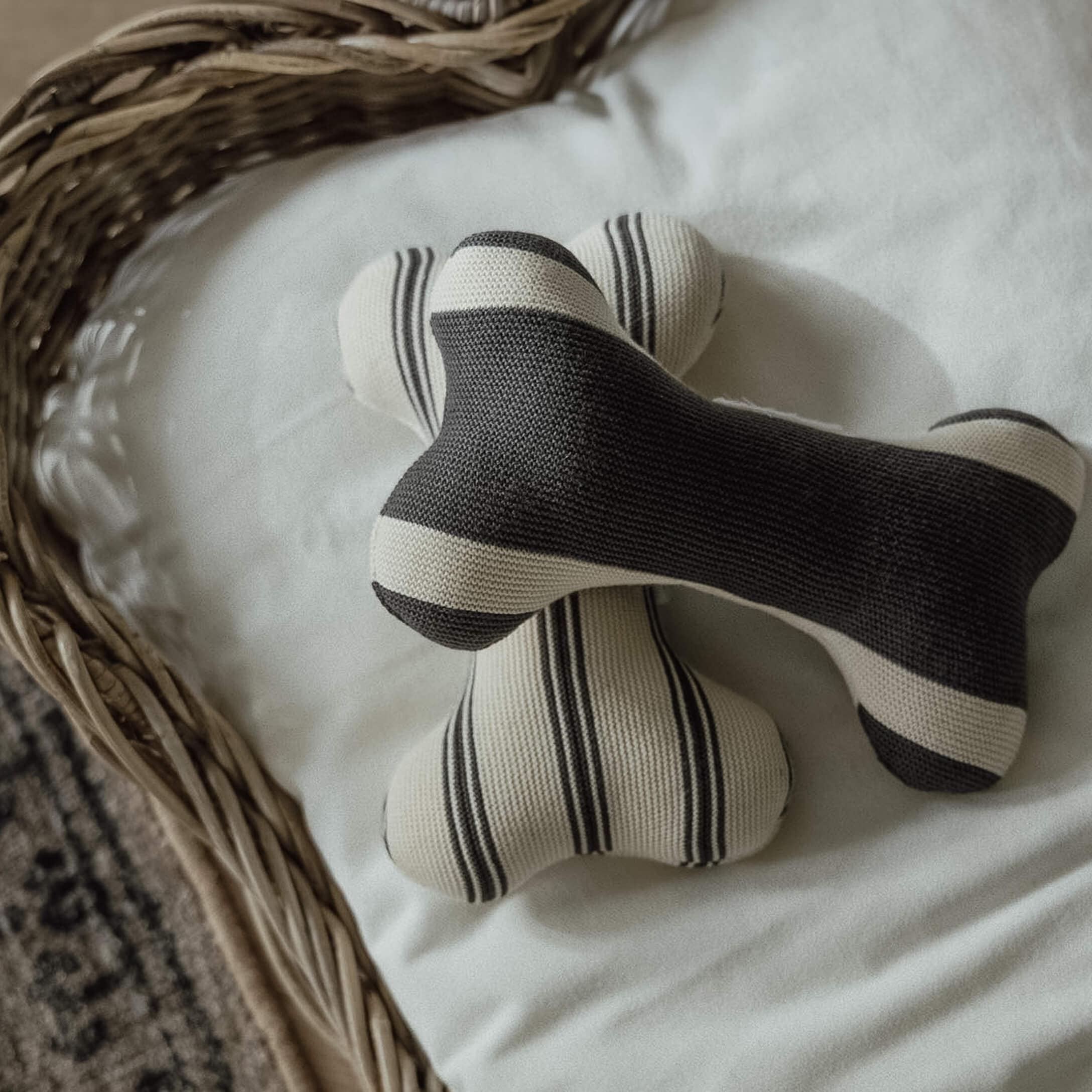 Zwei gestrickte Knochen-Spielzeuge mit schwarz-weißen Streifen auf weißem Hintergrund im Korb